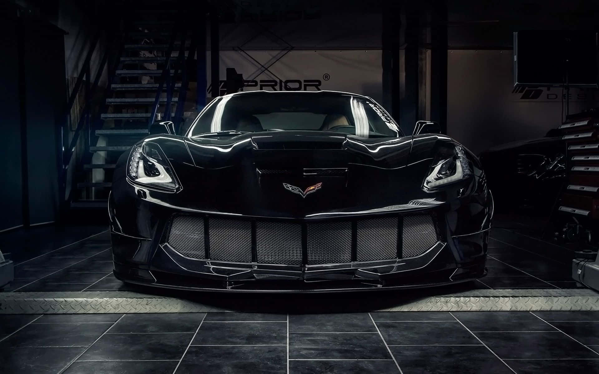 Chevrolet Corvette Stingray 桌布 壁紙 — 一輛時尚的黑色Corvette跑車在昏暗的車庫中，在戲劇性的燈光下閃閃發光，車庫舖有瓷磚地板並配有工業設備。