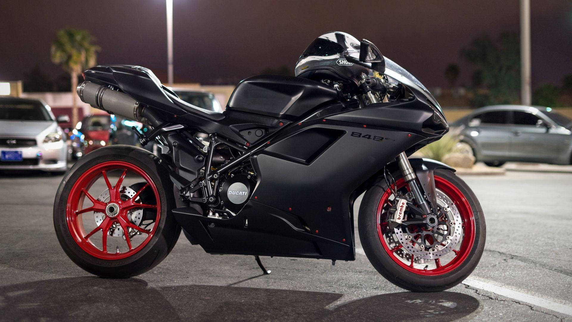 機車 桌布 壁紙 — 一輛時尚的黑色Ducati電單車，配以鮮紅色車輪，夜晚停在有燈光的停車場。