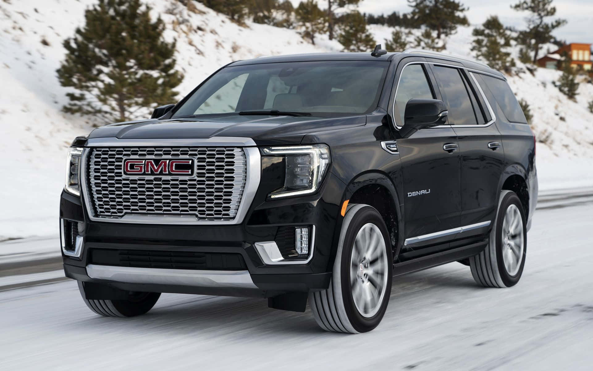 Gmc Yukon 桌布 壁紙 — 一輛時尚的黑色GMC Denali SUV自信地行駛在被白雪覆蓋、兩旁種滿常青樹的山路上。