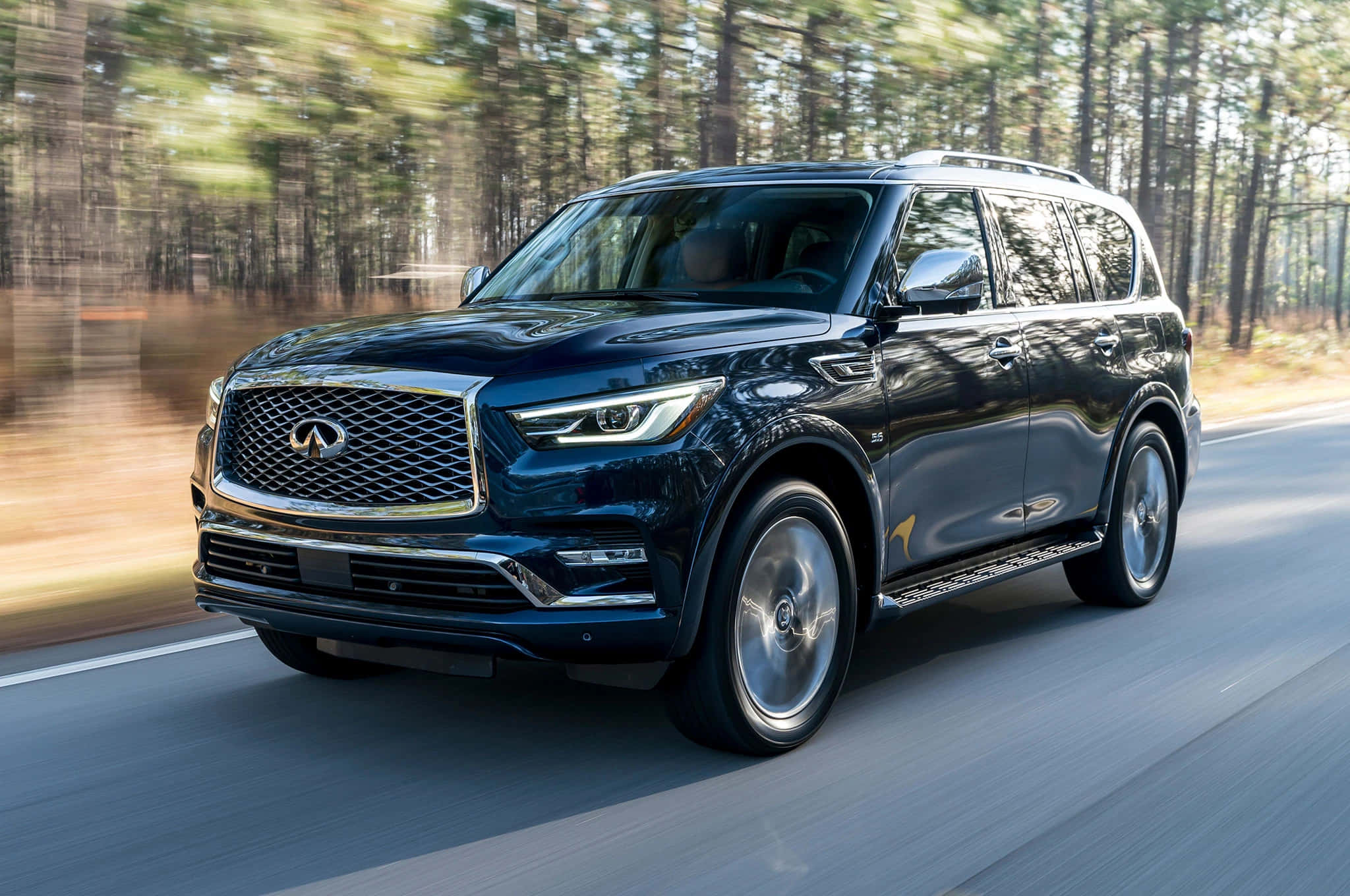 Infiniti Qx80 桌布 壁紙 — 一輛時尚的黑色Infiniti QX80 SUV在森林道路上行駛，動態模糊效果強調其動力與豪華感。