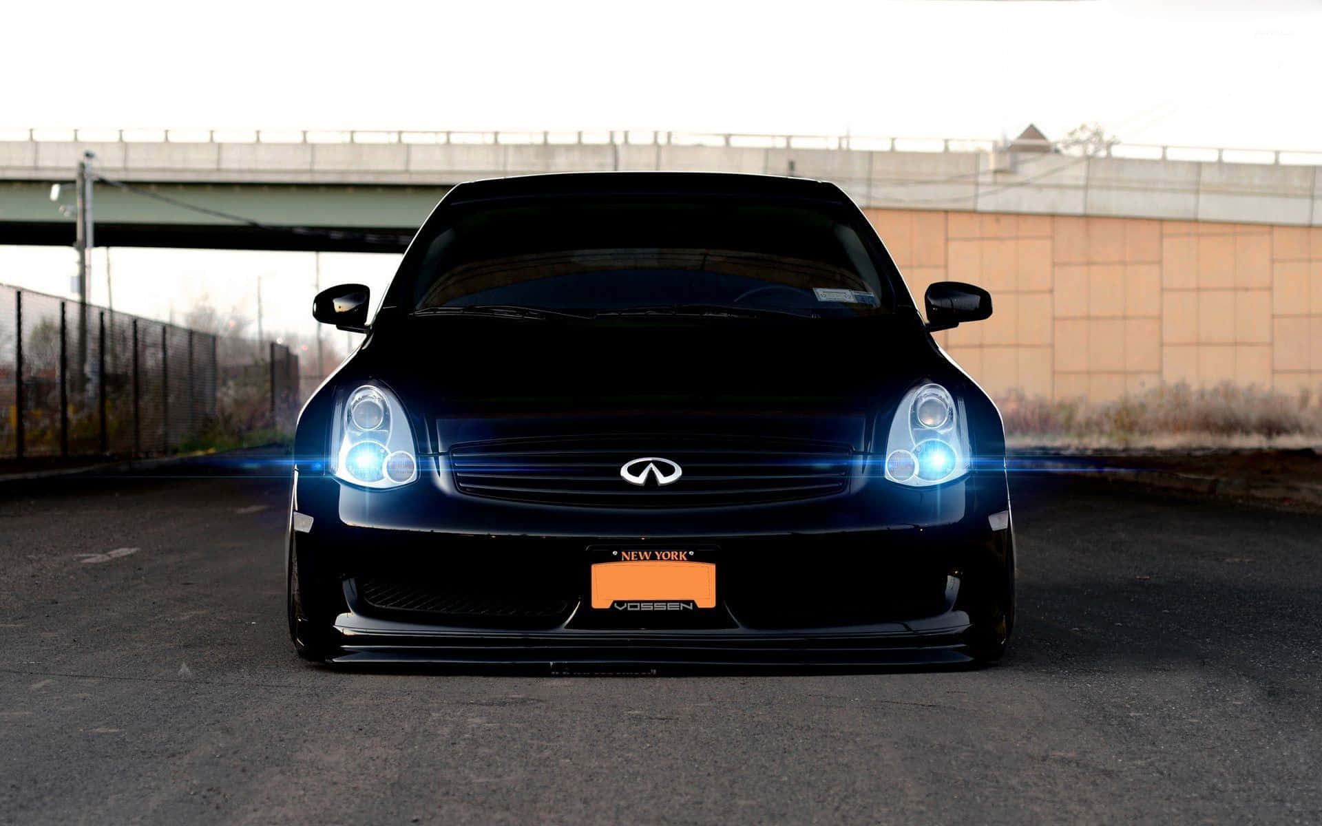 Infiniti G35 桌布 壁紙 — 一輛時尚的黑色Infiniti跑車，帶有發光的藍色車頭燈，停放在城市高架橋下。