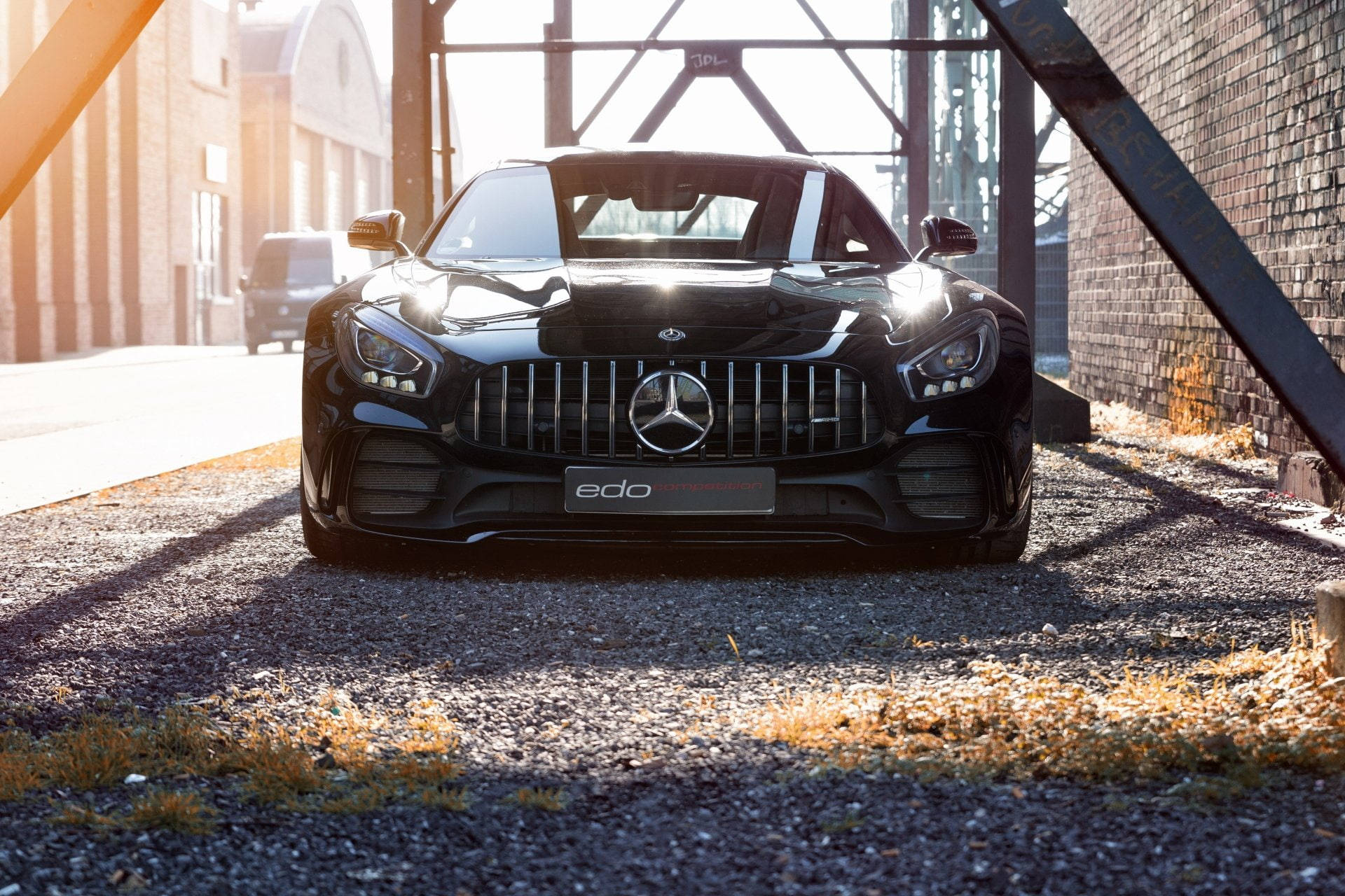 HD 桌布 壁紙 — 一輛時尚的黑色Mercedes-AMG GT停在工業鋼拱門下，金色陽光在礫石上投下長長的影子。