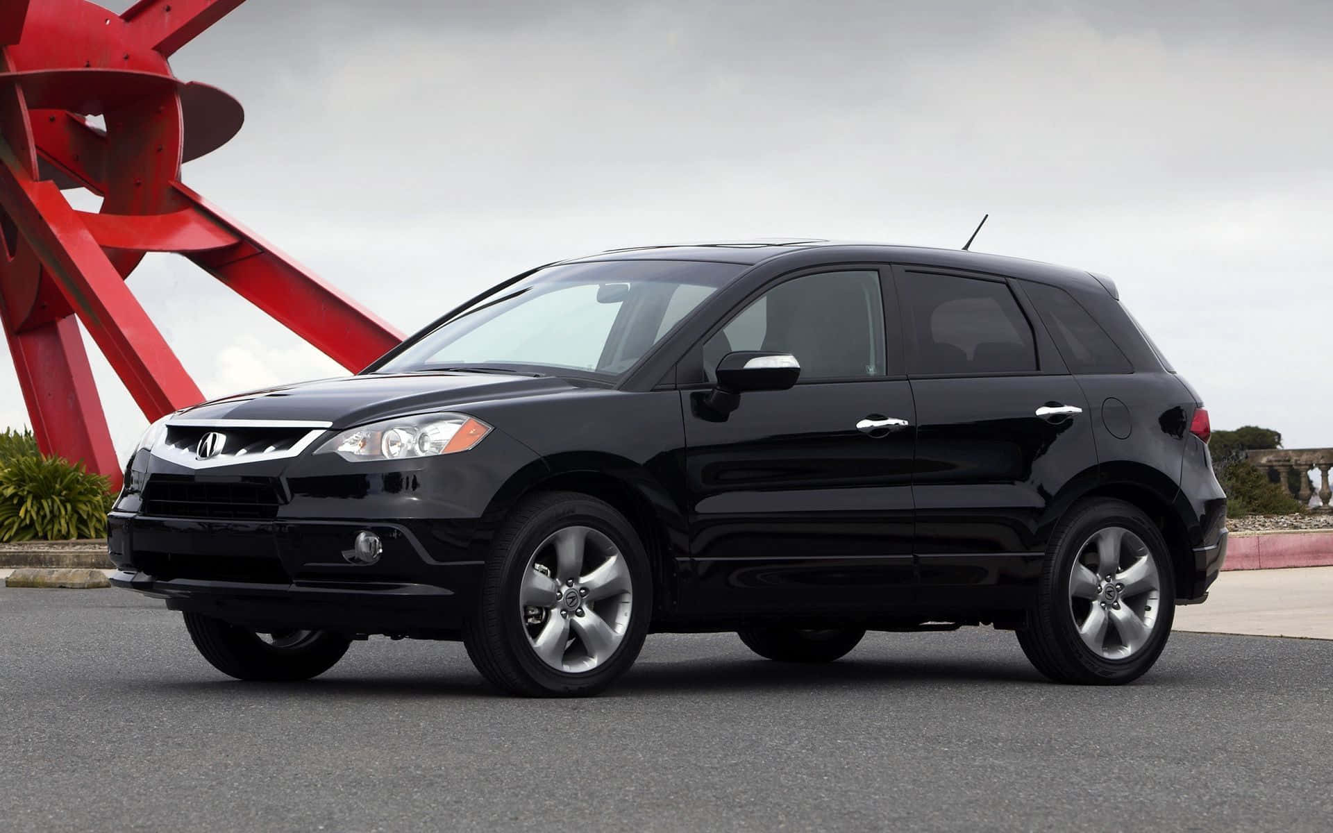 Acura Rdx 桌布 壁紙 — 一輛時尚的黑色SUV停在瀝青路上，背景是陰天，有一個巨大的紅色抽象雕塑。