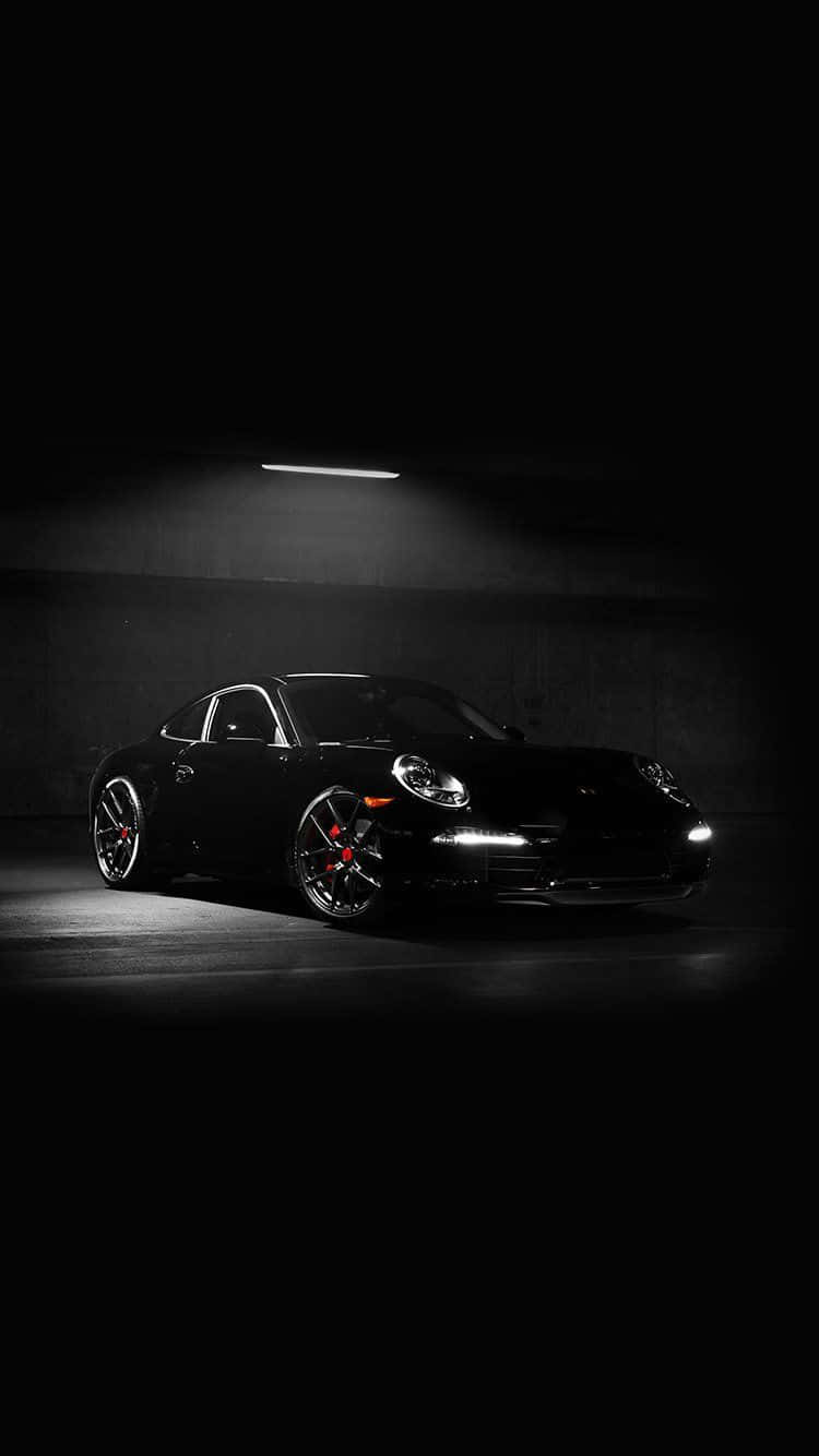 Porsche iPhone 桌布 壁紙 — 一輛時尚的黑色保時捷911雙門跑車，在黑暗的混凝土車庫中被單一頂燈照亮。