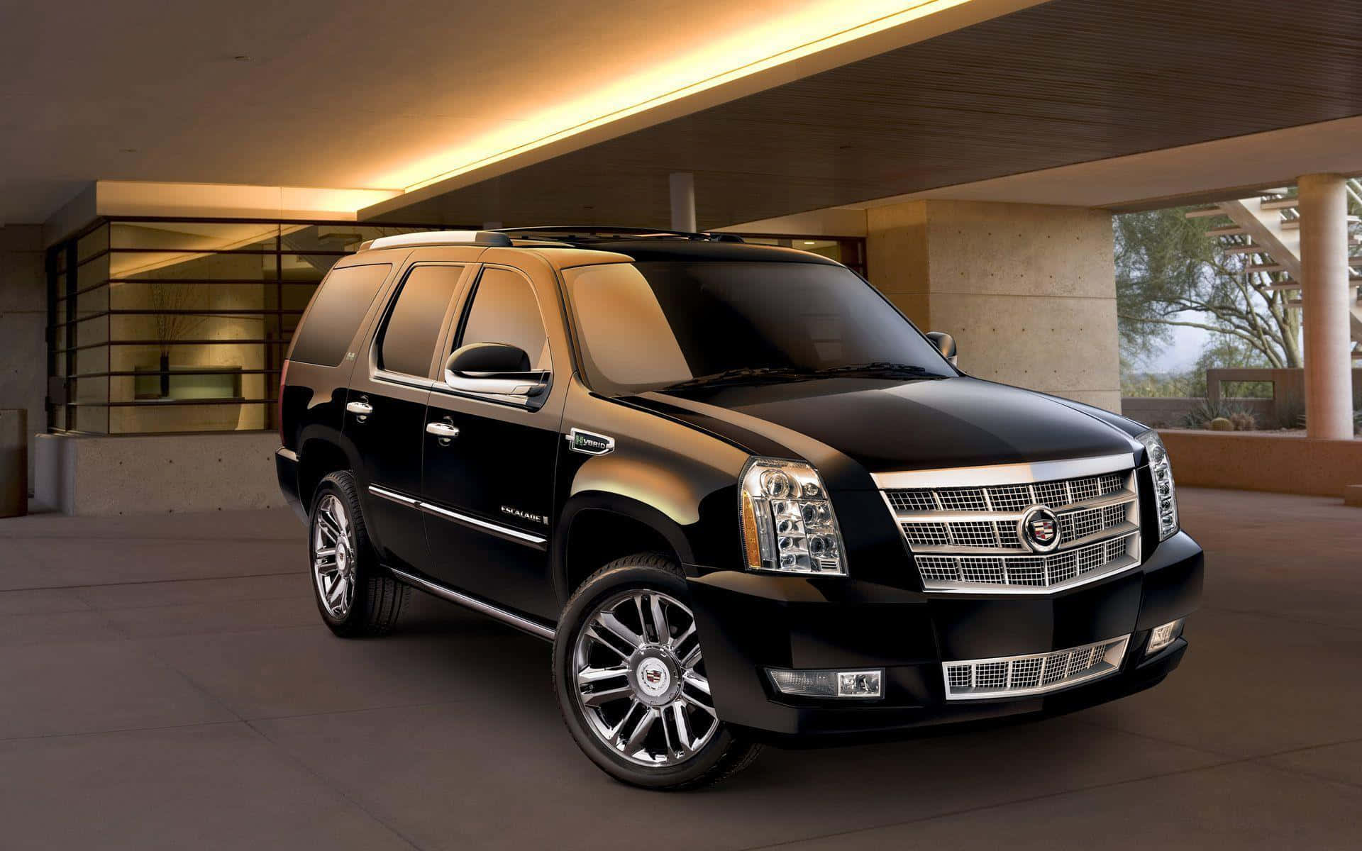 Cadillac Escalade 桌布 壁紙 — 一輛時尚的黑色凱迪拉克 Escalade SUV 在現代建築風格的車道上，於溫暖的頂燈下閃閃發光。