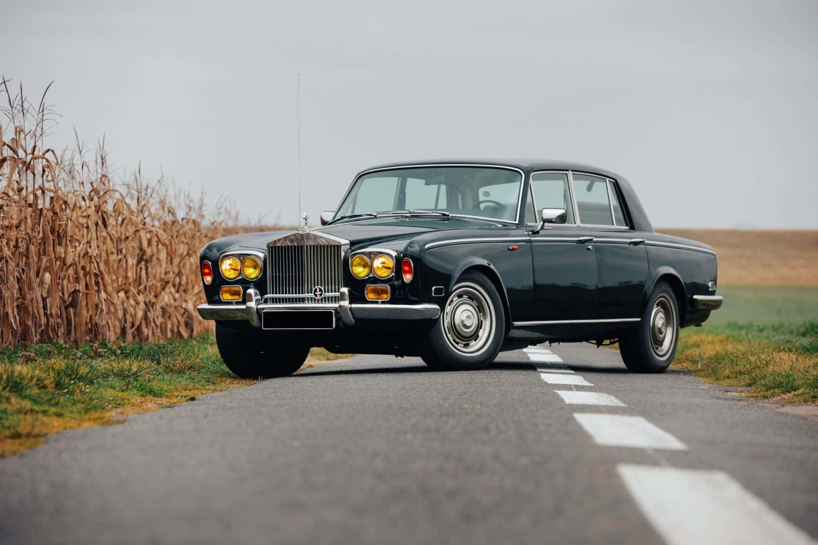 Bentley T2 桌布 壁紙 — 一輛時尚的黑色勞斯萊斯停泊在鄉村道路上，旁邊是乾燥的玉米稈田，天空多雲。