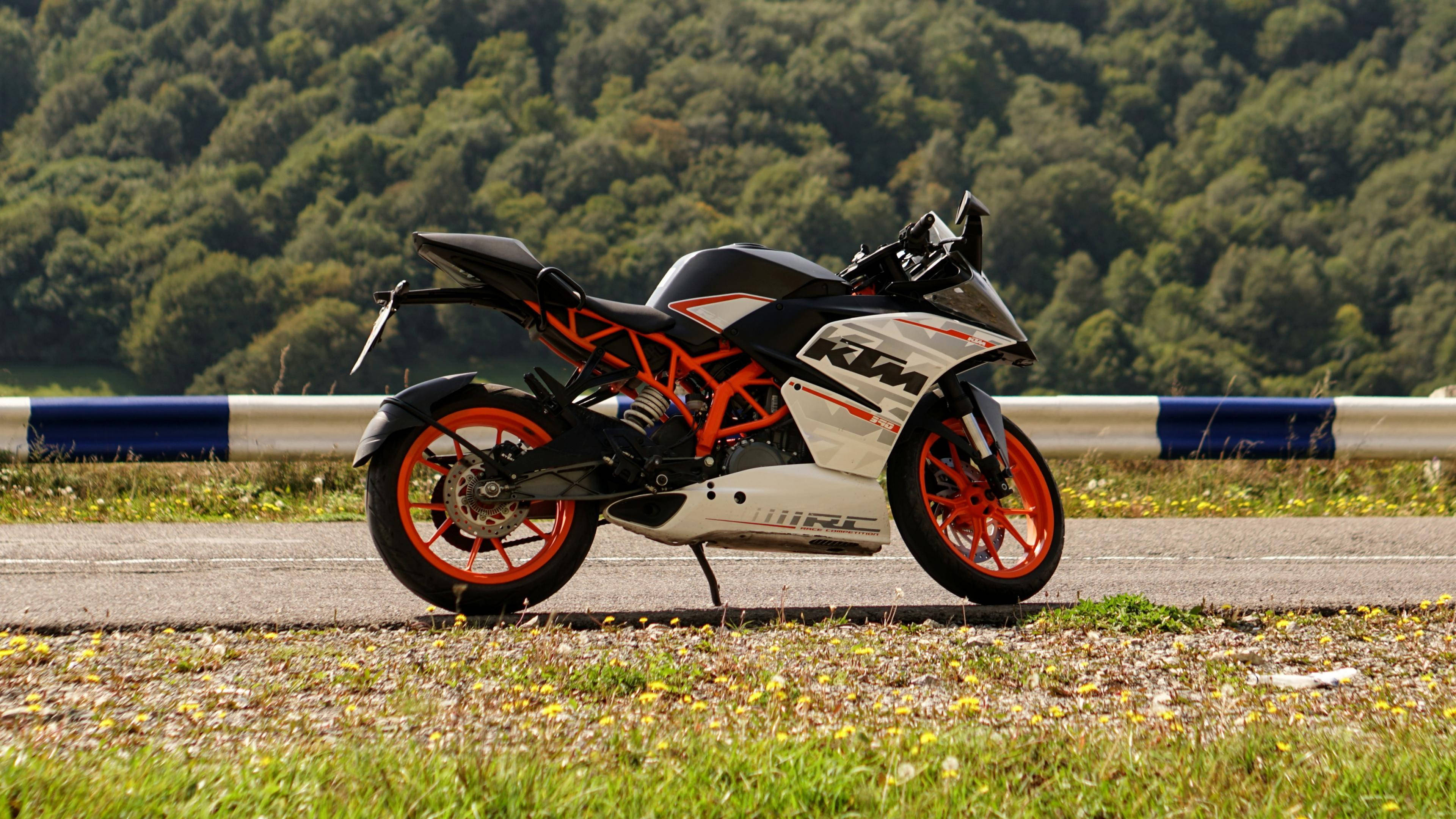ktm bikes 桌布 壁紙 — 一輛時尚的黑色和橙色KTM電單車停泊在路邊，背景是樹木繁茂的山丘。