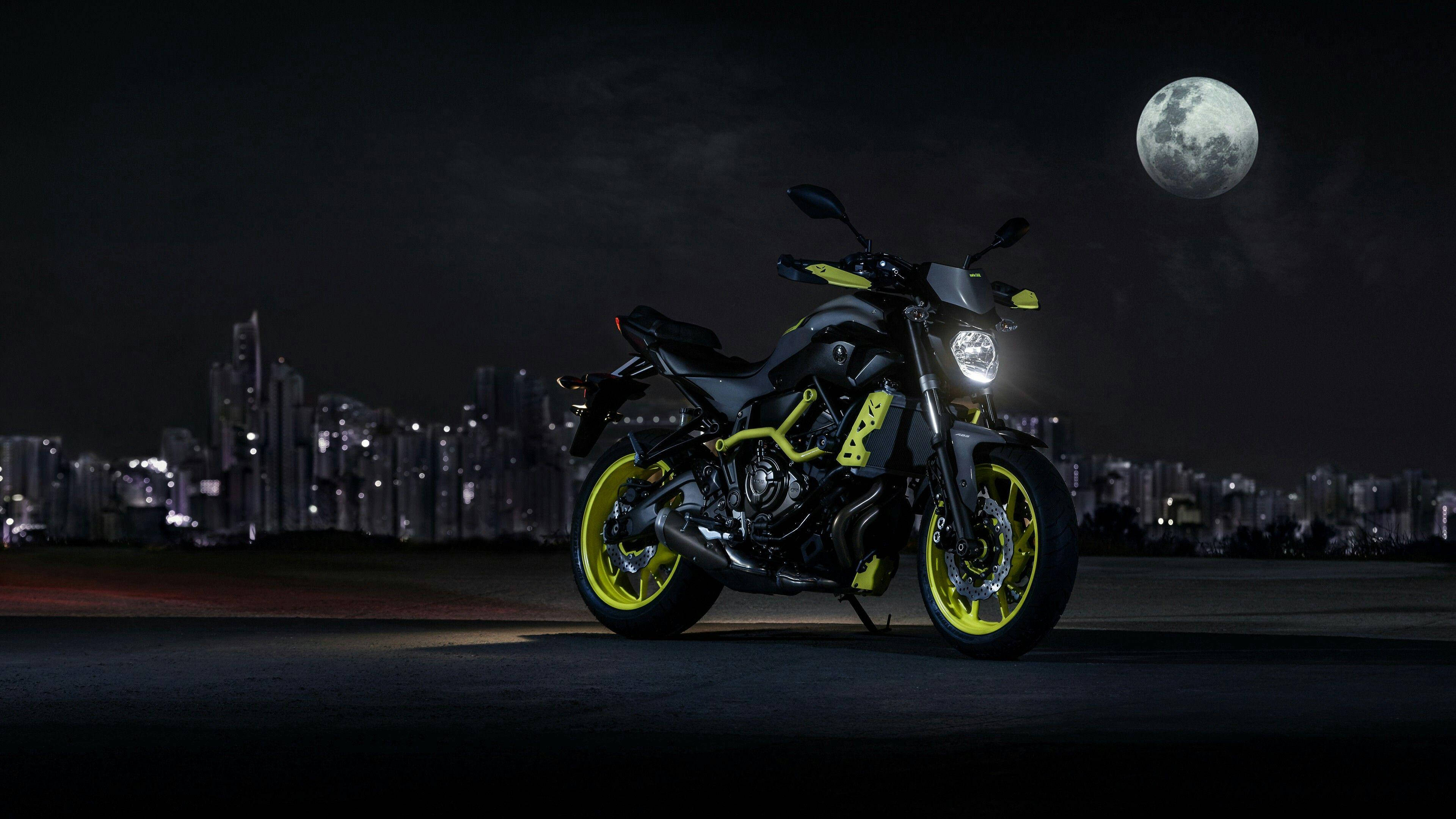 yamaha mt 15 桌布 壁紙 — 一輛時尚的黑色和螢光黃色電單車在滿月下閃耀，背景是夜晚發光的城市天際線。