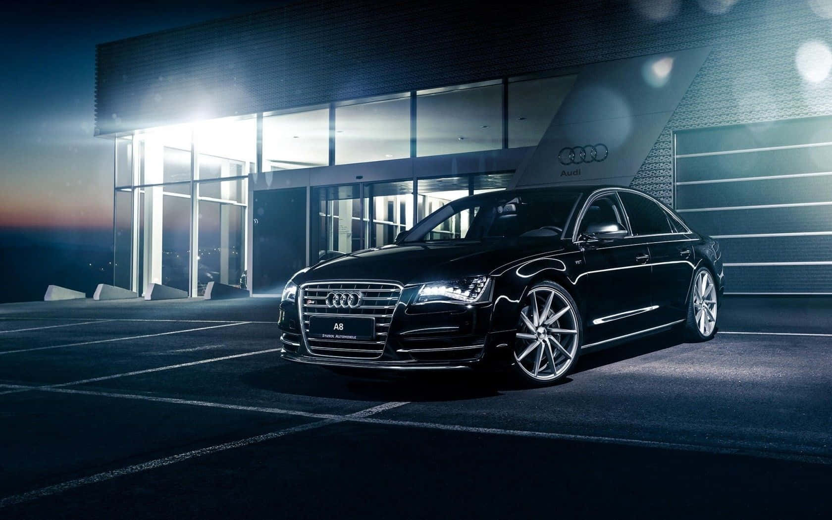 Audi S8 桌布 壁紙 — 一輛時尚的黑色奧迪A8轎車在現代玻璃建築前，於戲劇性的夜間燈光下閃閃發光。