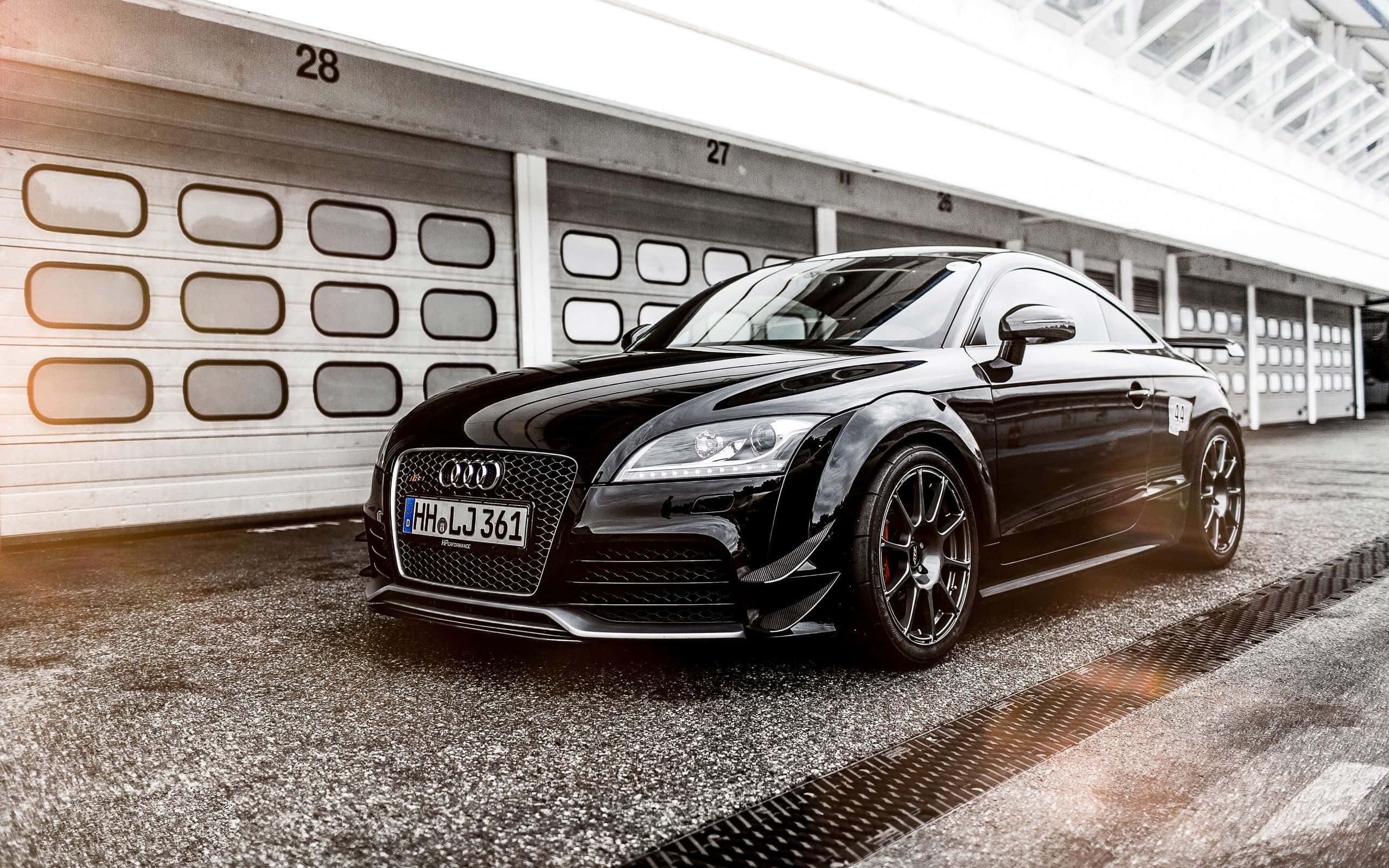 Audi Tt 桌布 壁紙 — 一輛時尚的黑色奧迪TT RS跑車停在有編號的車庫前，陽光在其光澤表面閃爍。