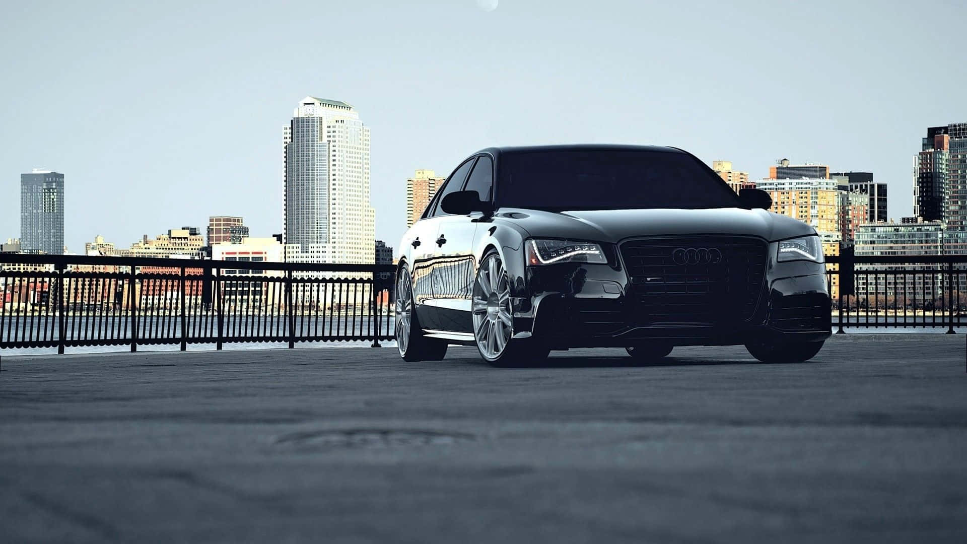 Audi S8 桌布 壁紙 — 一輛時尚的黑色奧迪房車停泊在城市天台，背景是現代化的天際線，天空晴朗。