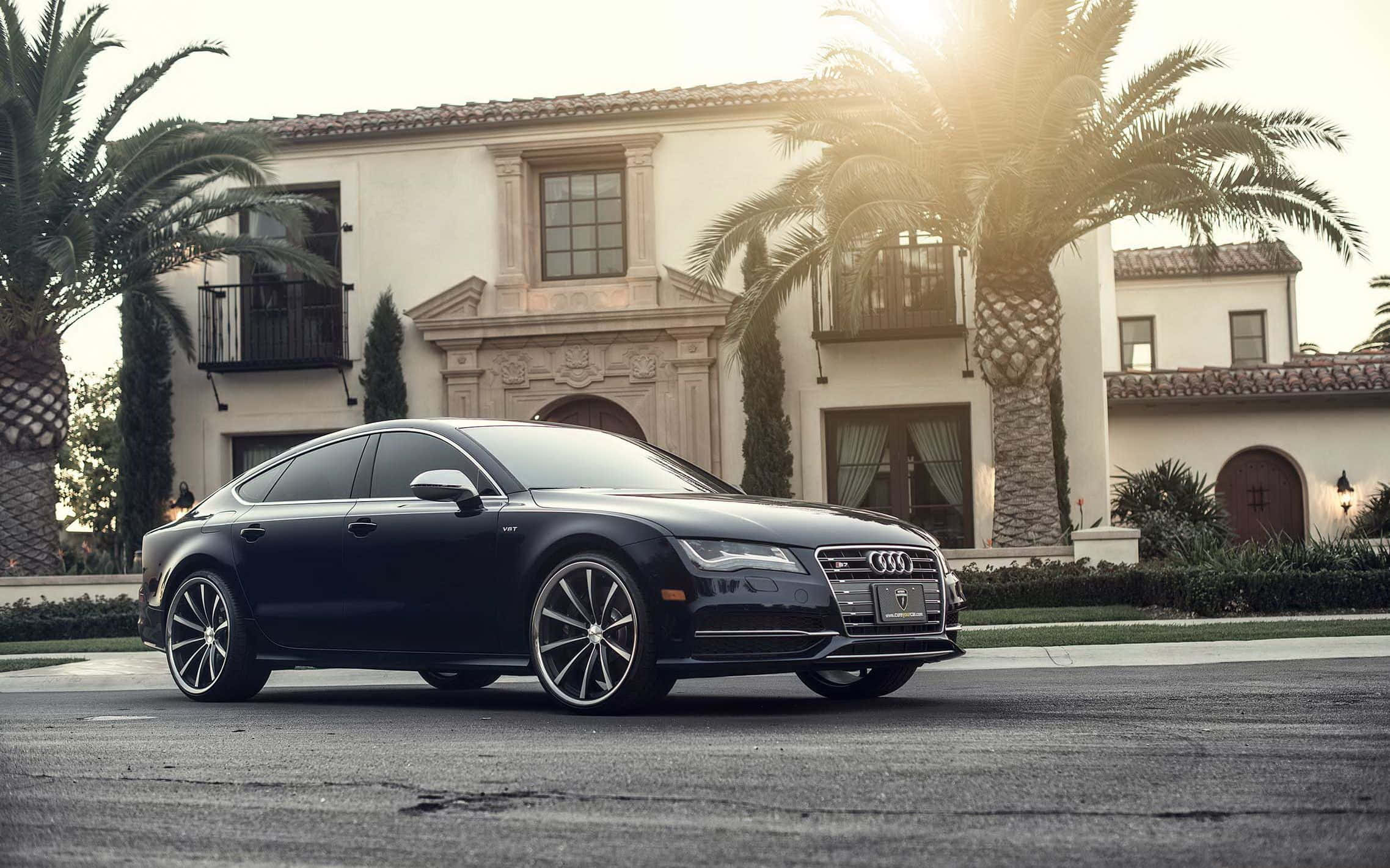 Audi S7 桌布 壁紙 — 一輛時尚的黑色奧迪轎車停在一棟豪華的西班牙風格豪宅前，周圍有棕櫚樹和溫暖的金色陽光。