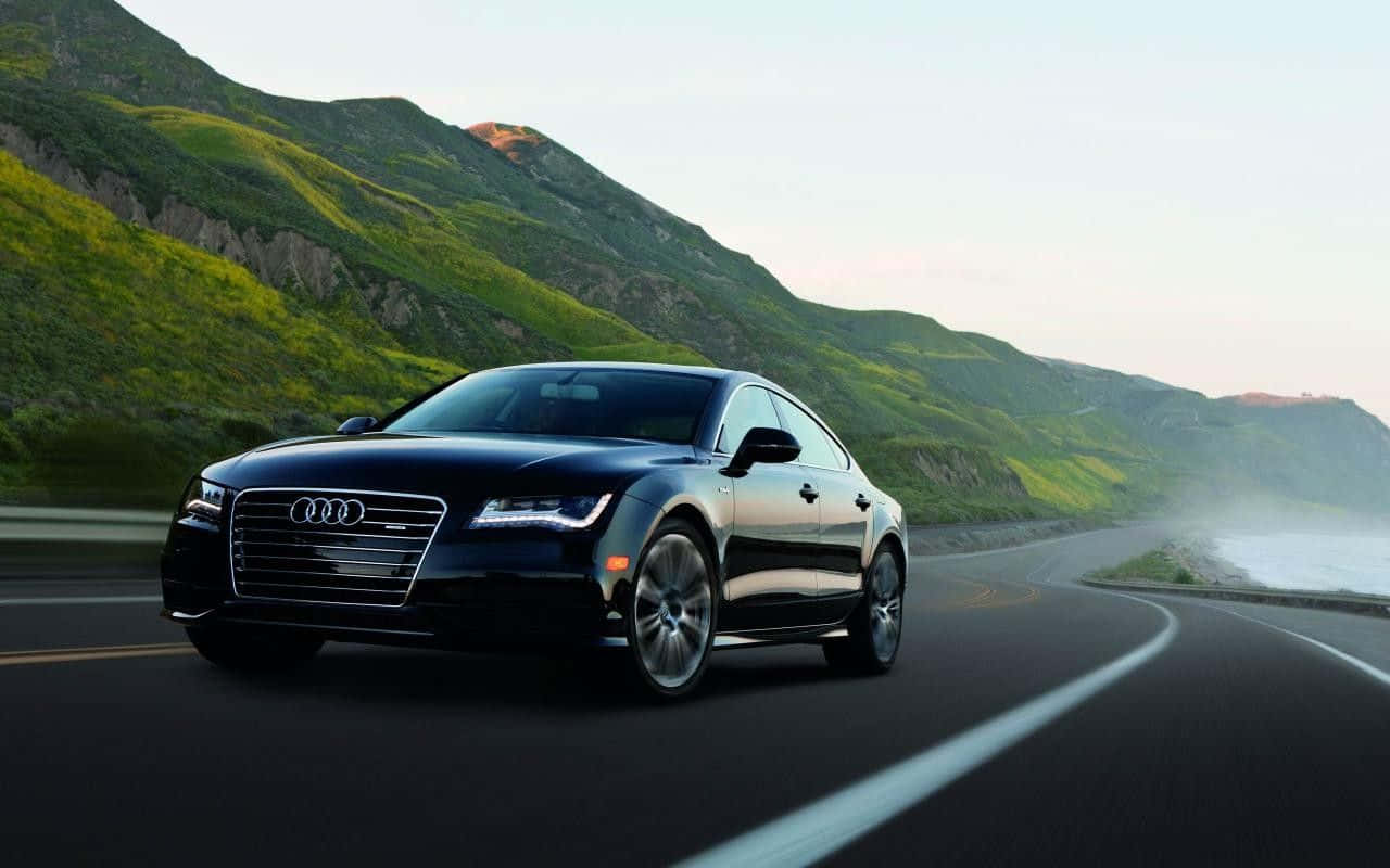 Audi S7 桌布 壁紙 — 一輛時尚的黑色奧迪轎車沿著蜿蜒的海岸公路行駛，兩旁是鬱鬱蔥蔥的綠色山丘和海霧。