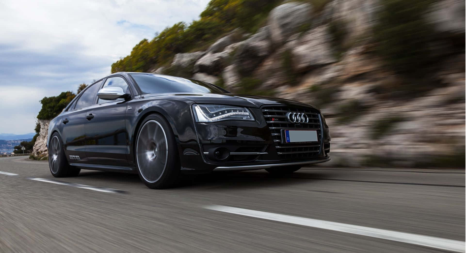 Audi S8 桌布 壁紙 — 一輛時尚的黑色奧迪轎車沿著蜿蜒的山路疾馳，背景是模糊的岩石懸崖和綠植。