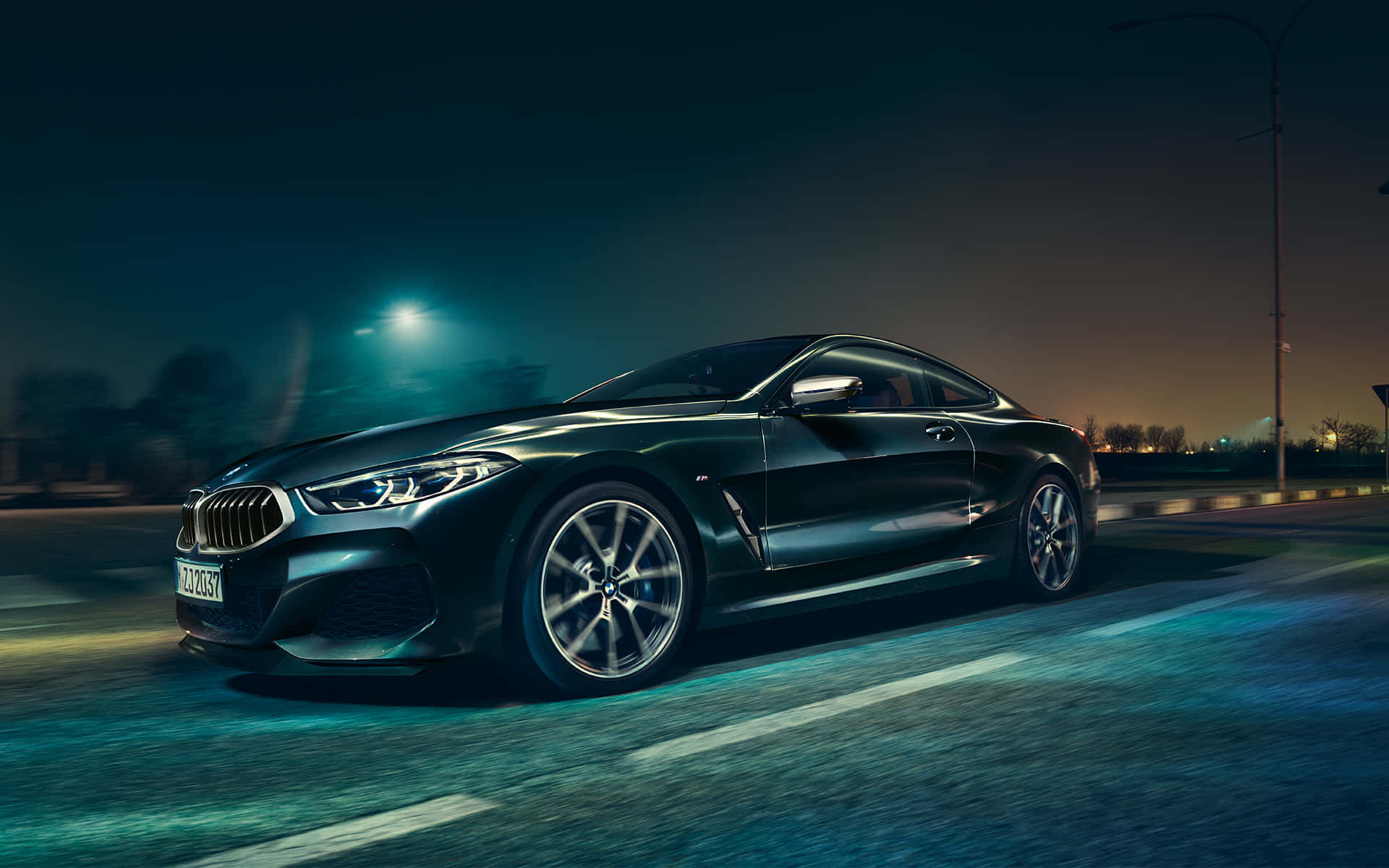 Bmw 8 Series 桌布 壁紙 — 一輛時尚的黑色寶馬轎跑車在夜間於潮濕的道路上，在發光的街燈下行駛，帶有動態模糊效果。