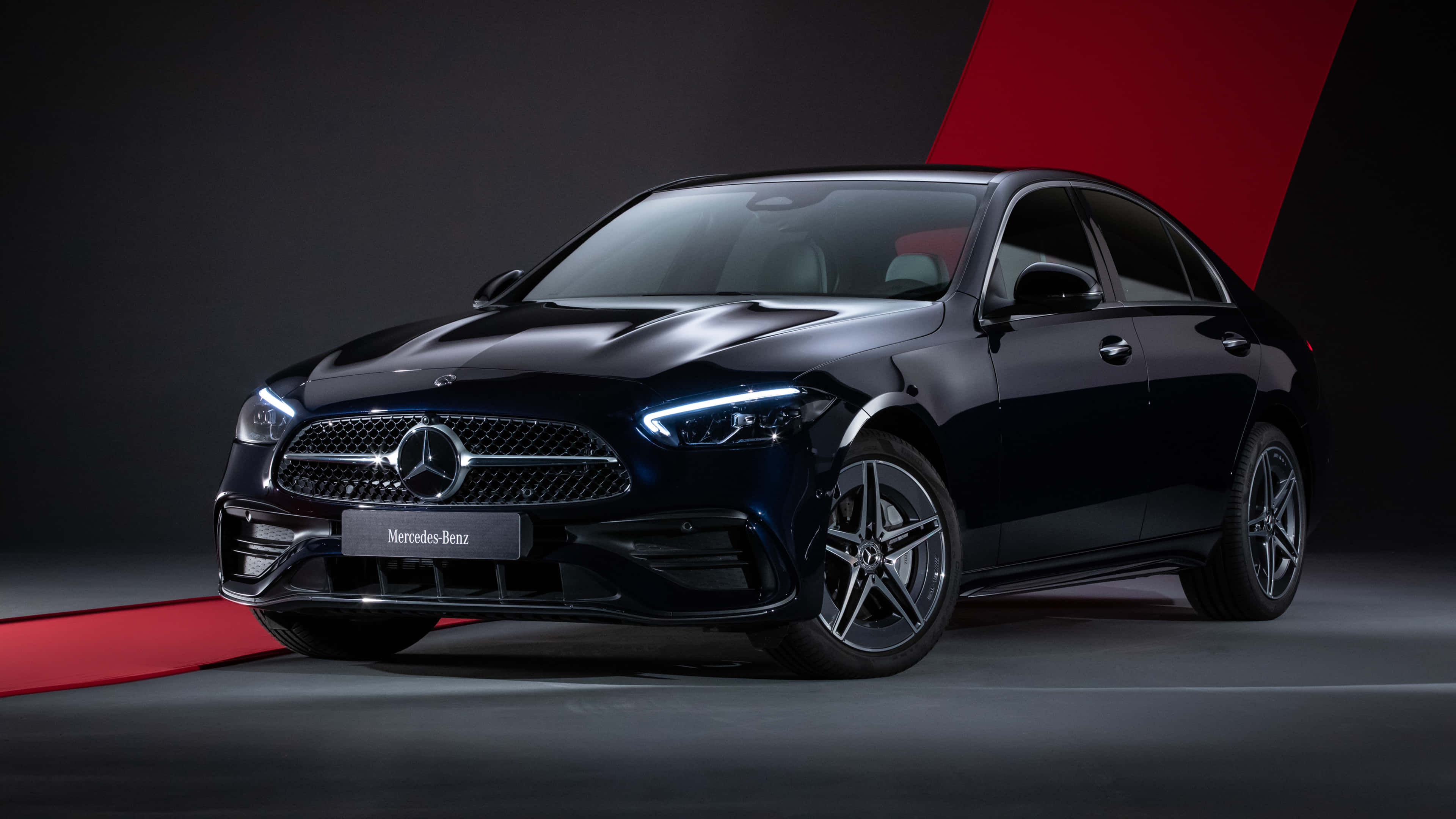 4K Mercedes 桌布 壁紙 — 一輛時尚的黑色平治房車在攝影棚燈光下閃耀，帶有紅色點綴，背景為深色。