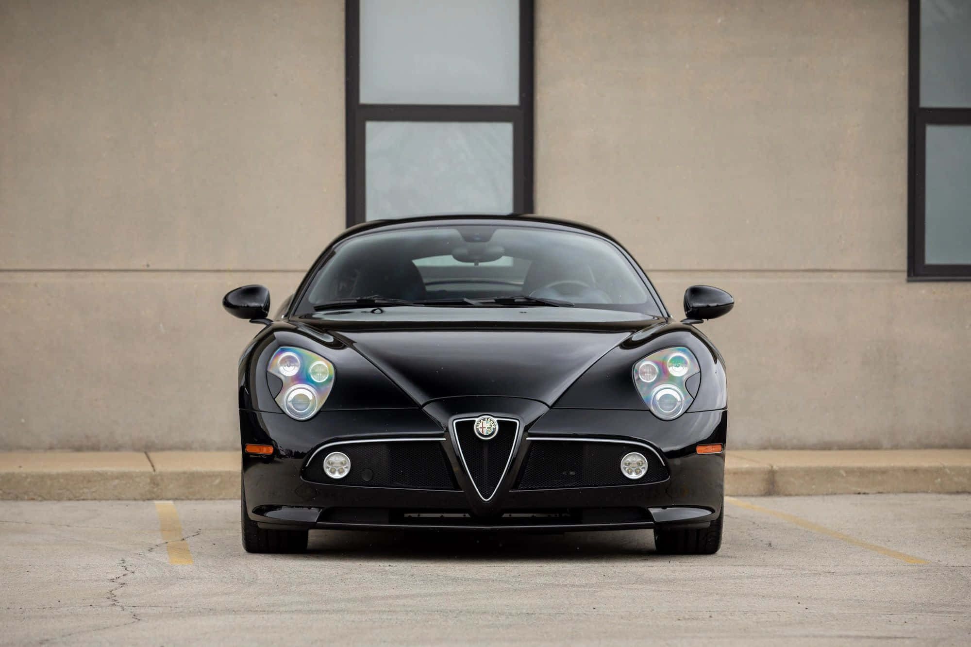 Alfa Romeo 8c Competizione 桌布 壁紙 — 一輛時尚的黑色愛快羅密歐跑車在停車場面向前方，背景是樸素的米色建築。