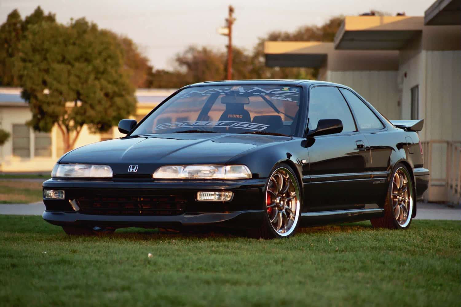 Honda Integra 桌布 壁紙 — 一輛時尚的黑色改裝本田轎跑車在黃金時段停放在草地上，配備定制輪轂和賽車貼花。
