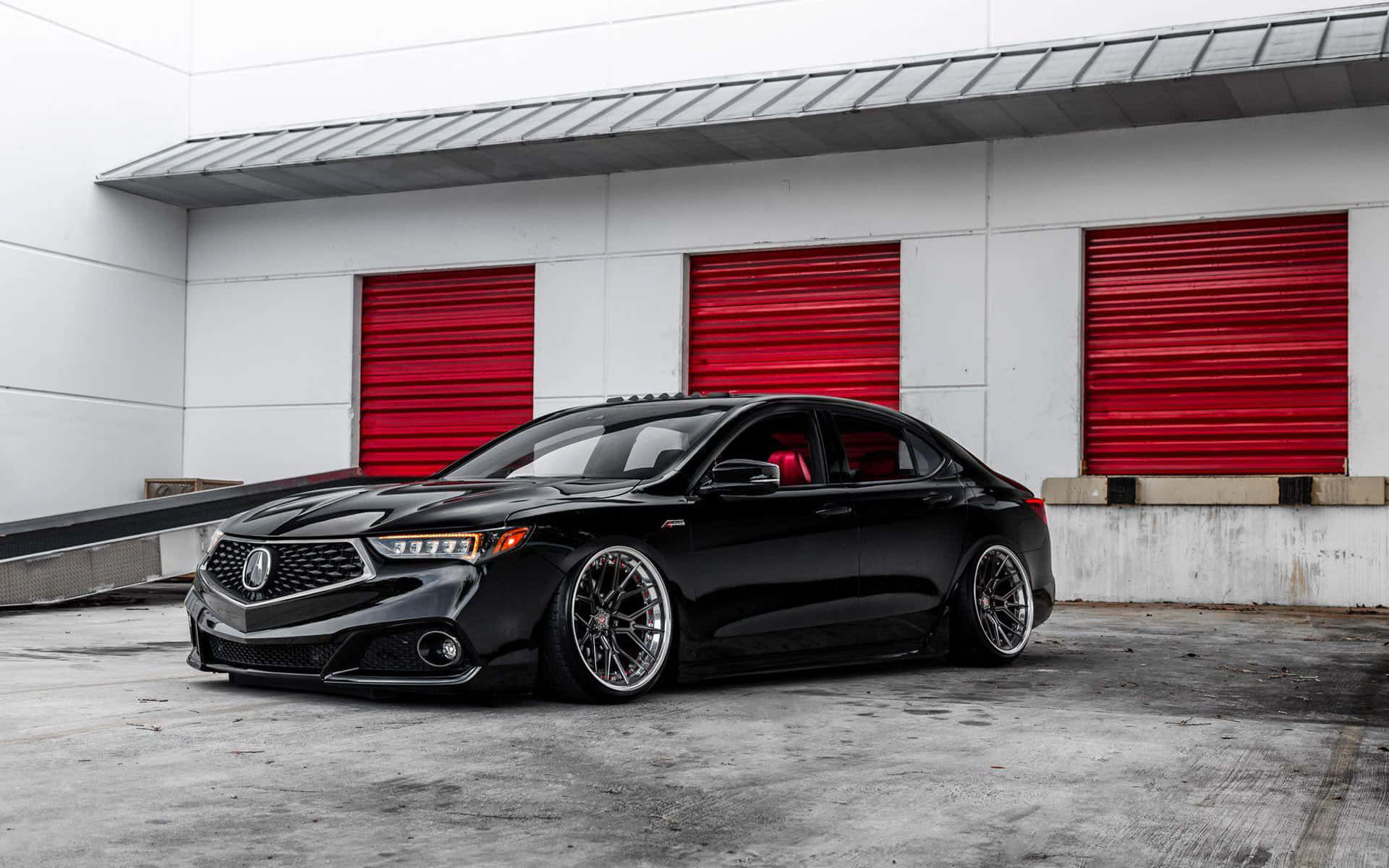 Acura Tlx 桌布 壁紙 — 一輛時尚的黑色改裝轎車配備定制輪圈，停在帶有醒目紅色捲簾門的白色建築前。