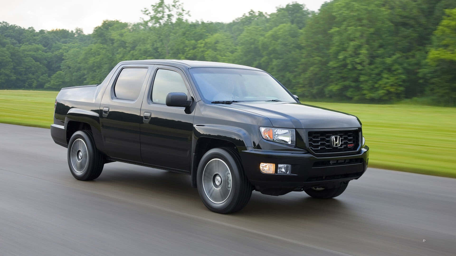 Honda Ridgeline 桌布 壁紙 — 一輛時尚的黑色本田Ridgeline皮卡在鋪砌的道路上行駛，背景中茂密的綠色樹木和草地模糊不清。