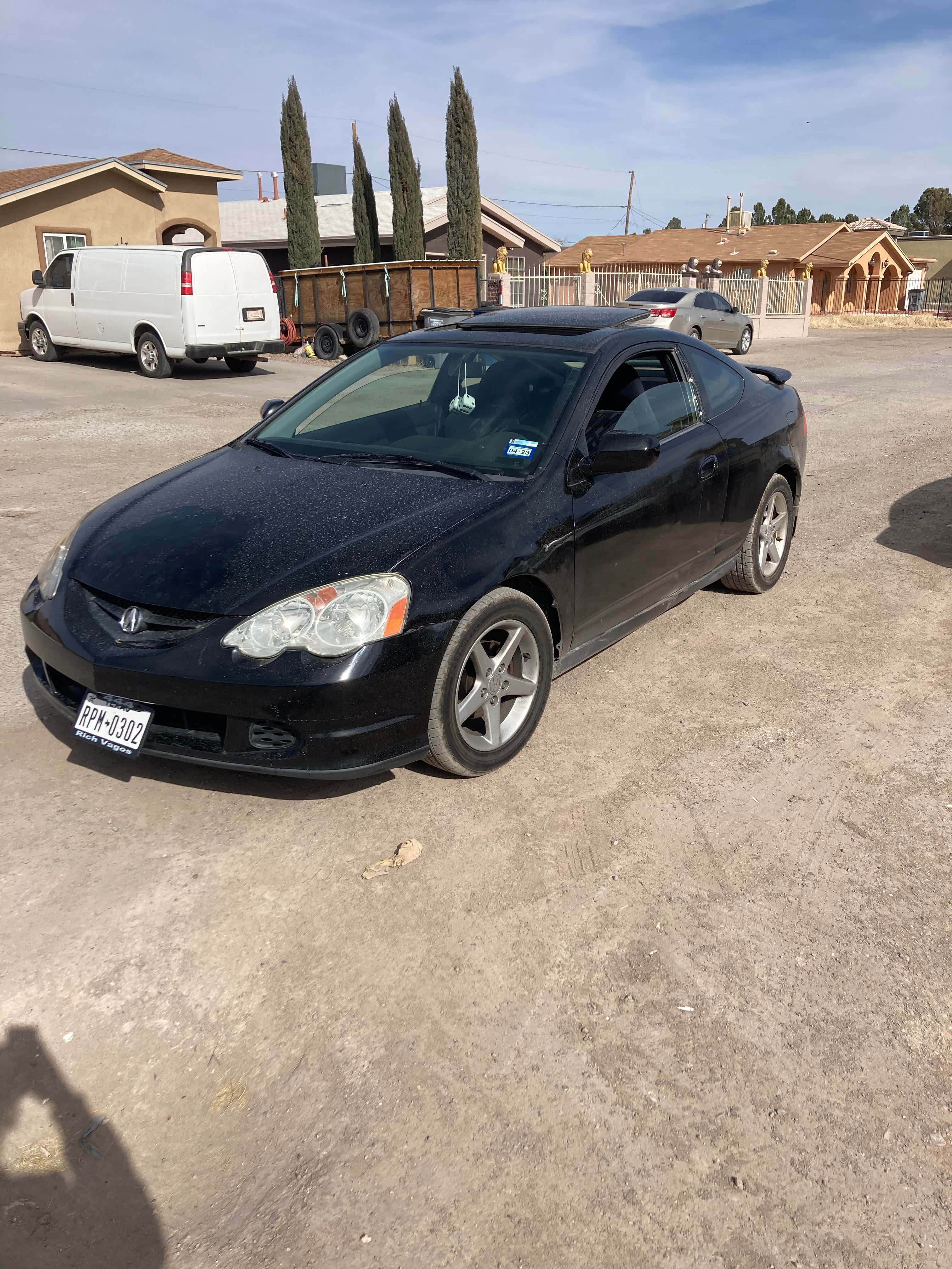 Acura Rsx 桌布 壁紙 — 一輛時尚的黑色本田轎跑車停在塵土飛揚的地面上，背景是郊區房屋和高大的柏樹，天空清澈湛藍。