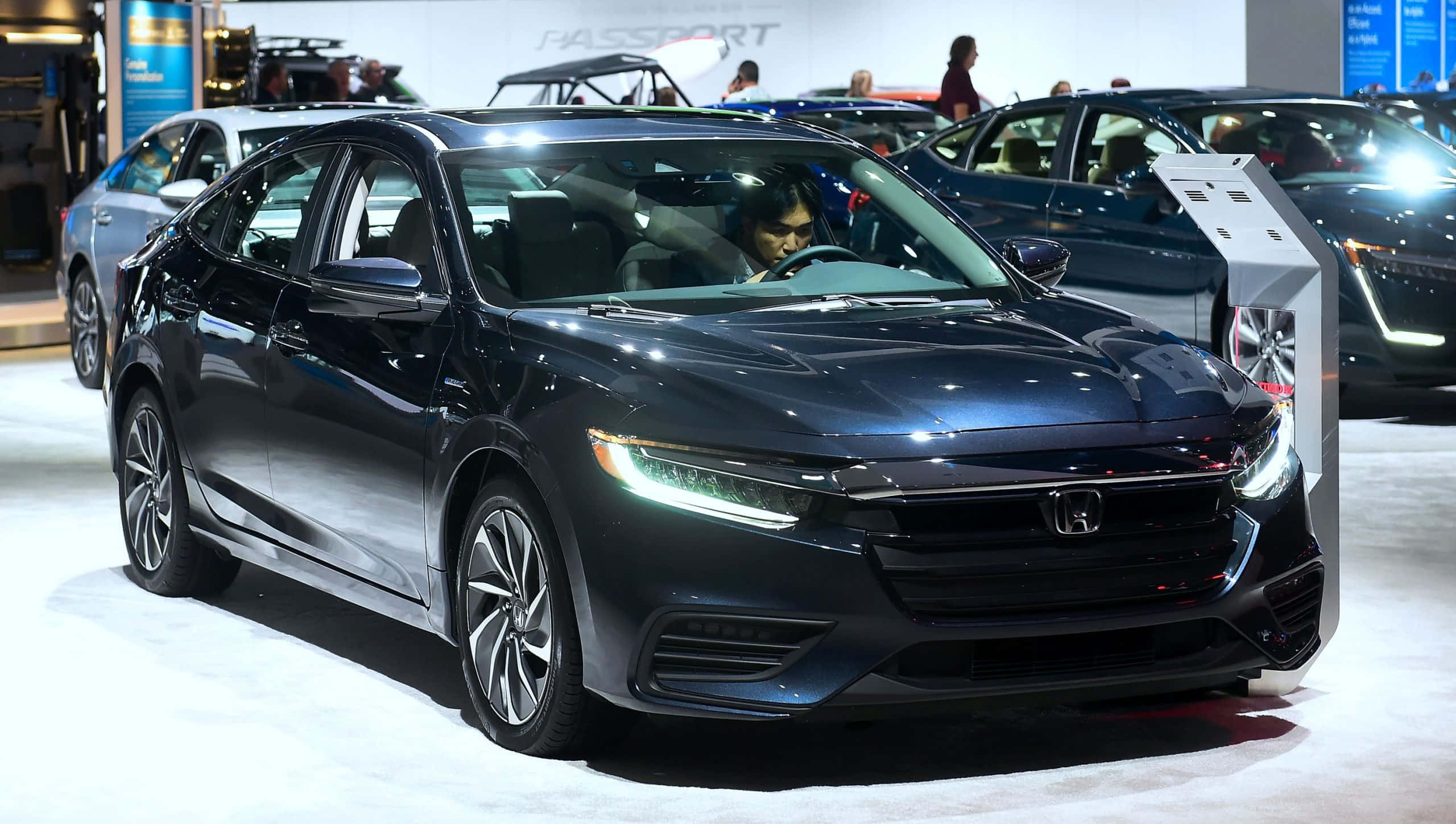 Honda Insight 桌布 壁紙 — 一輛時尚的黑色本田轎車在明亮的展廳燈光下閃閃發光，車內坐著一個人，在車展上。