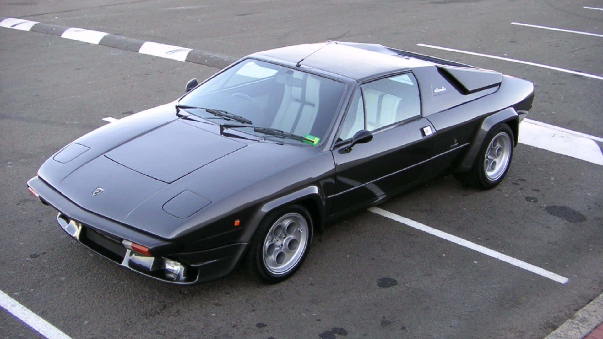 Lamborghini Silhouette 桌布 壁紙 — 一輛時尚的黑色林寶堅尼Countach斜泊在鋪有白線的瀝青停車場上。