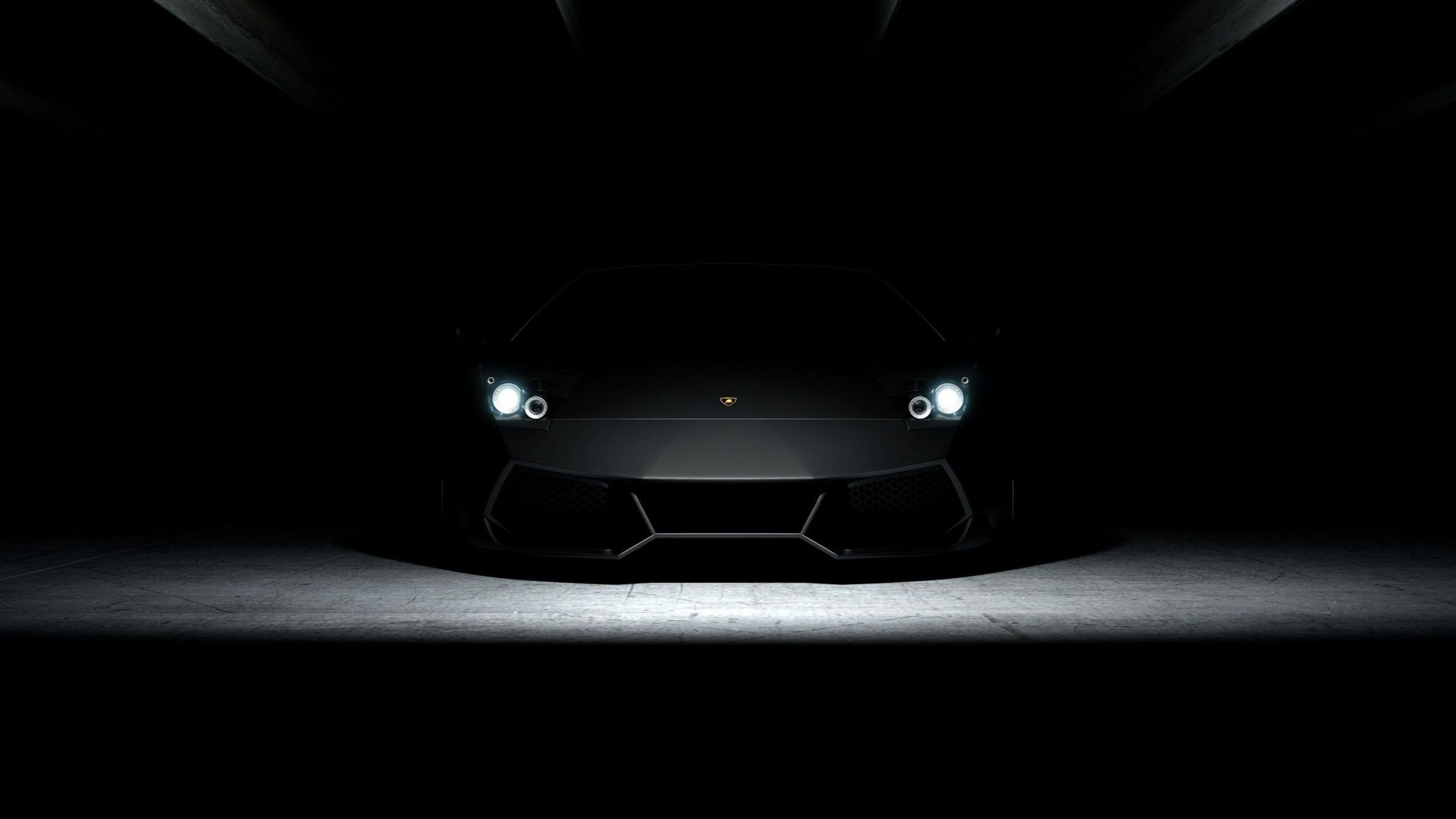 4K Car 桌布 壁紙 — 一輛時尚的黑色林寶堅尼跑車，在黑暗的地下車庫中被聚光燈照亮。