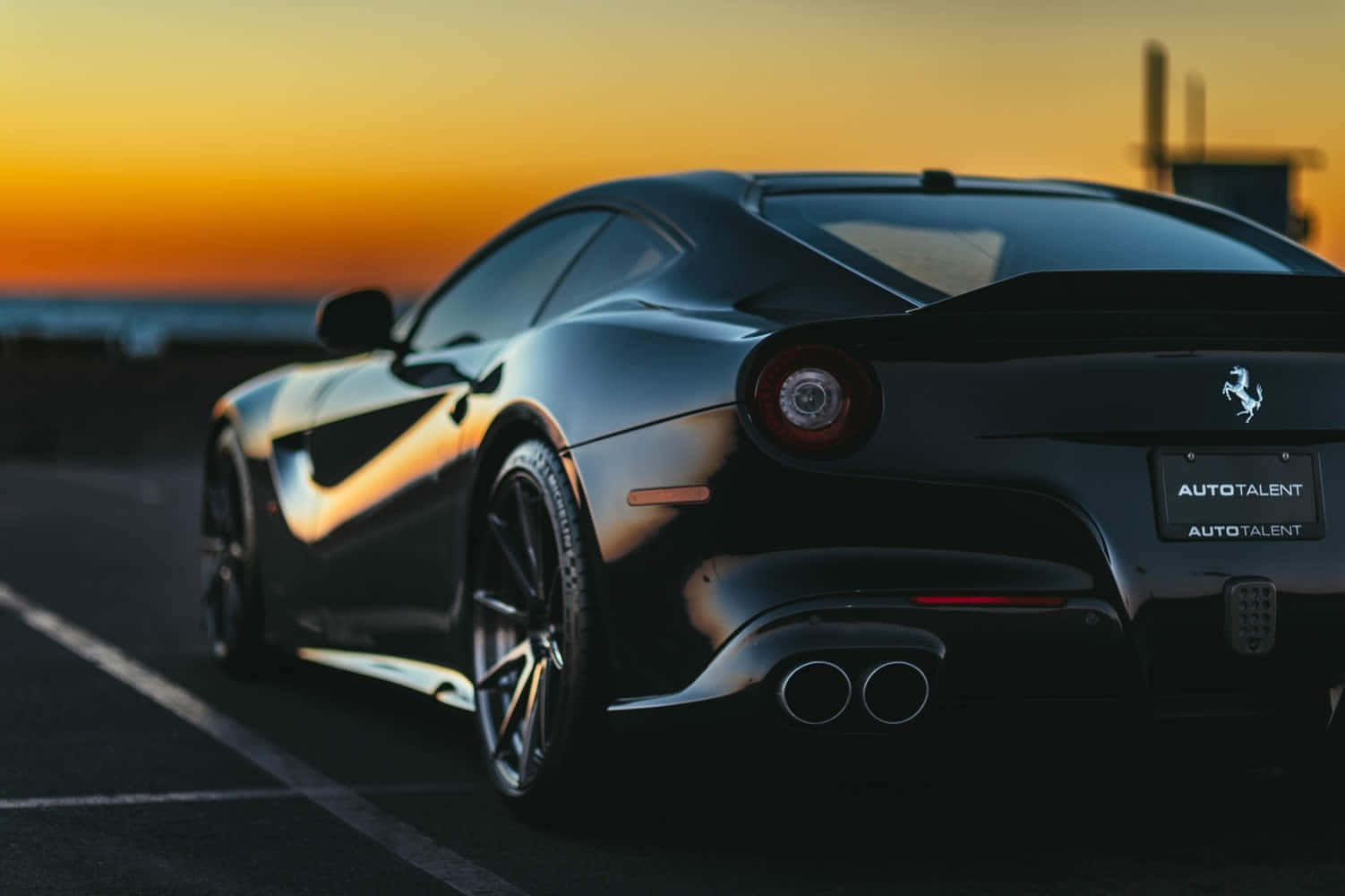 Ferrari F12 Berlinetta 桌布 壁紙 — 一輛時尚的黑色法拉利跑車停在日落時分的道路上，金色天空在其光澤表面反射。
