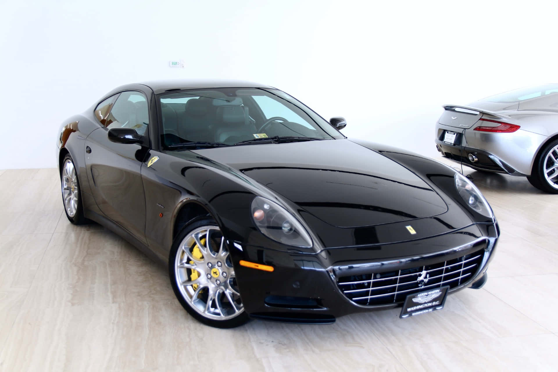 Ferrari 612 Scaglietti 桌布 壁紙 — 一輛時尚的黑色法拉利跑車配備黃色制動卡鉗，在明亮的白色工作室中展示，地板為淺色木地板。