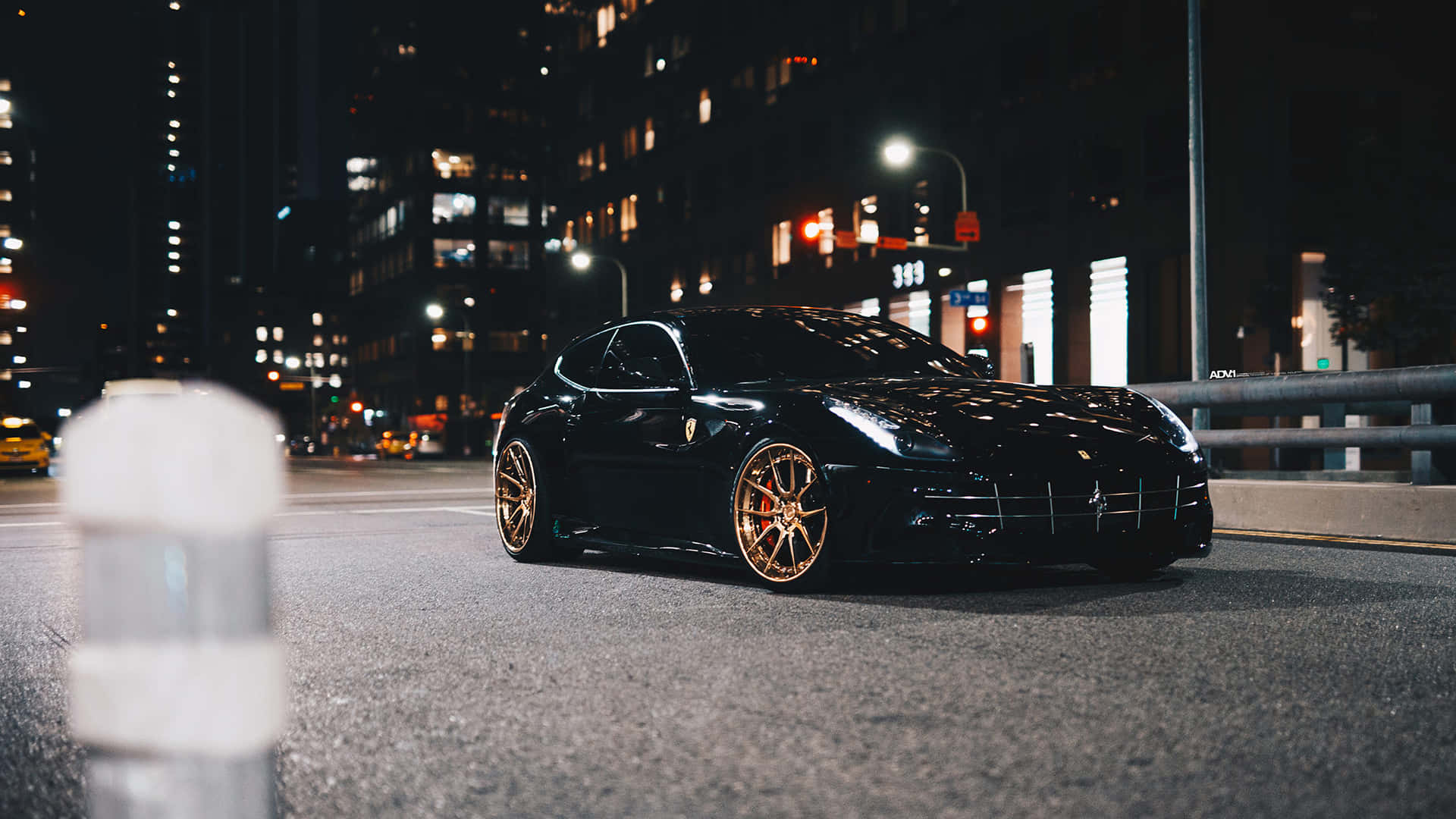 Ferrari Ff 桌布 壁紙 — 一輛時尚的黑色法拉利配金色輪圈，夜晚停泊在城市街道上，被街燈和建築物窗戶照亮。