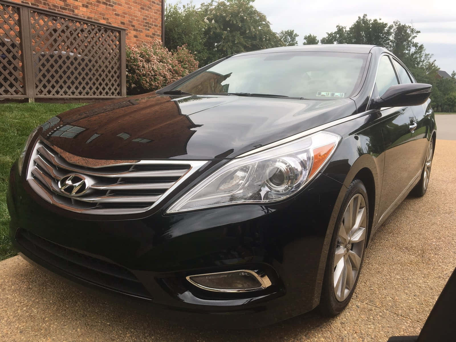 Hyundai Azera 桌布 壁紙 — 一輛時尚的黑色現代轎車在陰天閃閃發光，停在磚房和綠色草坪旁的礫石車道上。