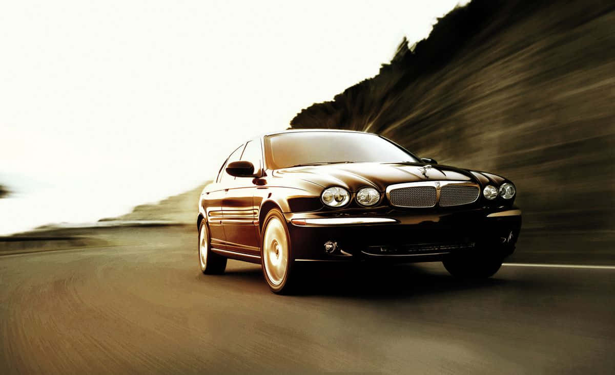Jaguar X-type 桌布 壁紙 — 一輛時尚的黑色積架房車沿著蜿蜒的海岸道路飛馳，動態模糊效果強調了速度。