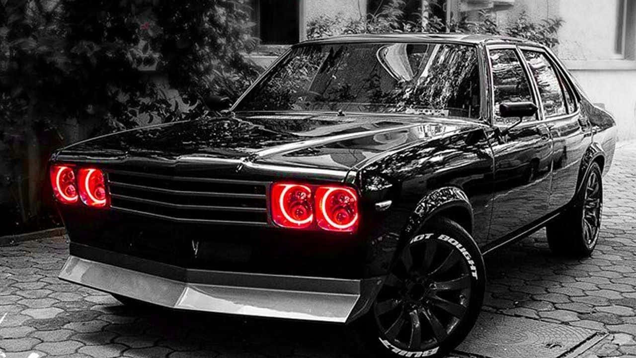 Hindustan Motors 桌布 壁紙 — 一輛時尚的黑色經典汽車，帶有發光的紅色圓形頭燈，停在鵝卵石街道上。