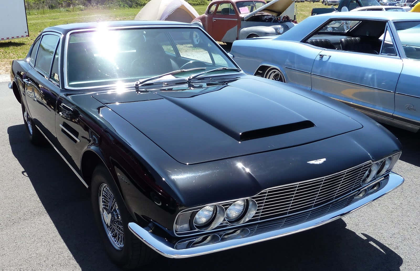 Car Hood 桌布 壁紙 — 一輛時尚的黑色經典阿斯頓馬丁，帶有鍍鉻裝飾，在車展的明亮陽光下閃閃發光。