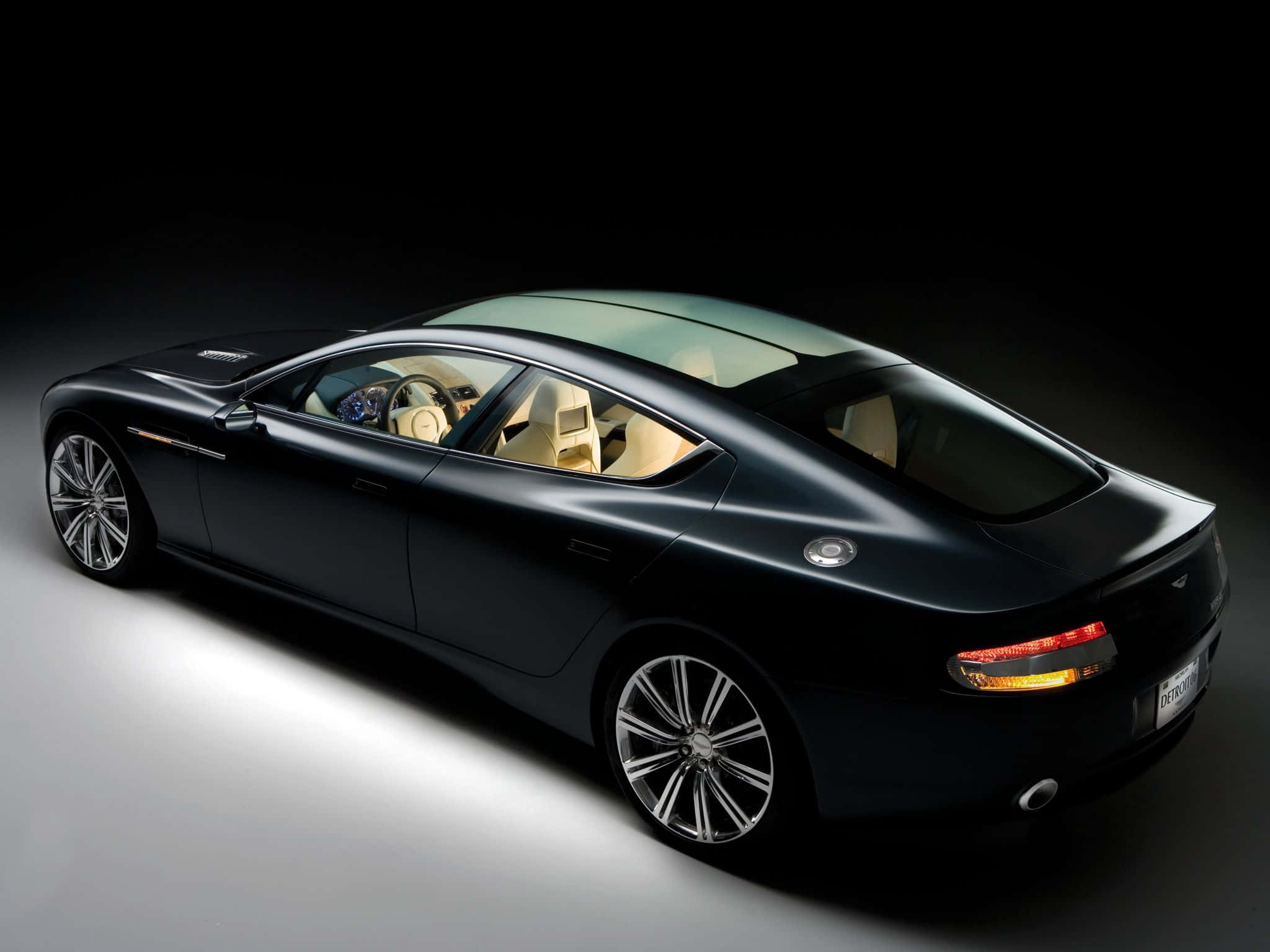 Aston Martin Rapide S 桌布 壁紙 — 一輛時尚的黑色豪華轎車，配以奶油色內飾，在深色背景的攝影棚燈光下閃耀。