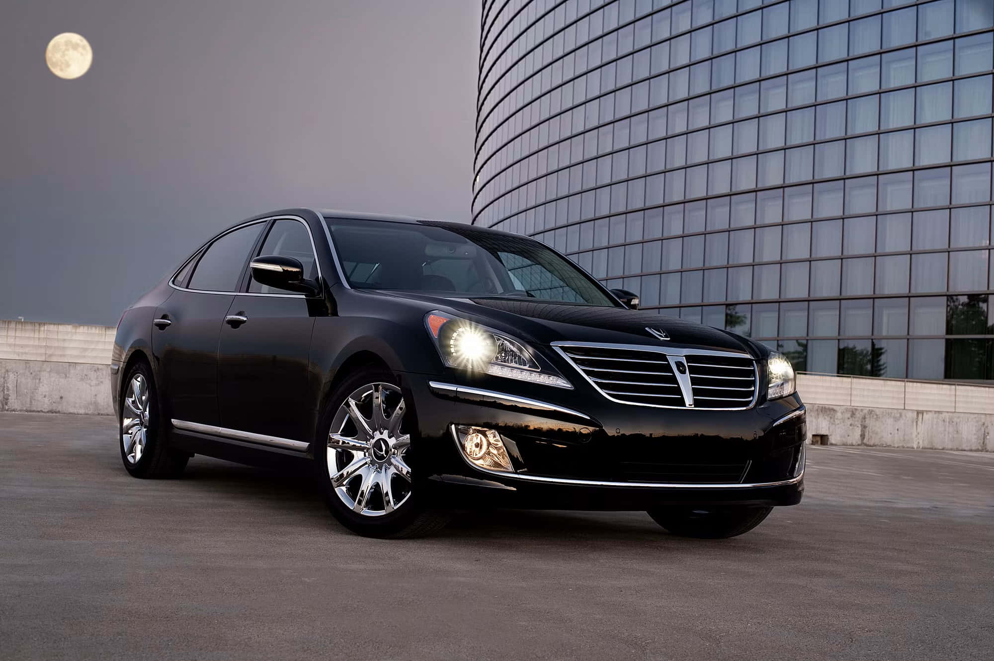Hyundai Equus 桌布 壁紙 — 一輛時尚的黑色豪華轎車在月光下閃閃發光，旁邊是一座現代玻璃建築，車頭燈亮著。