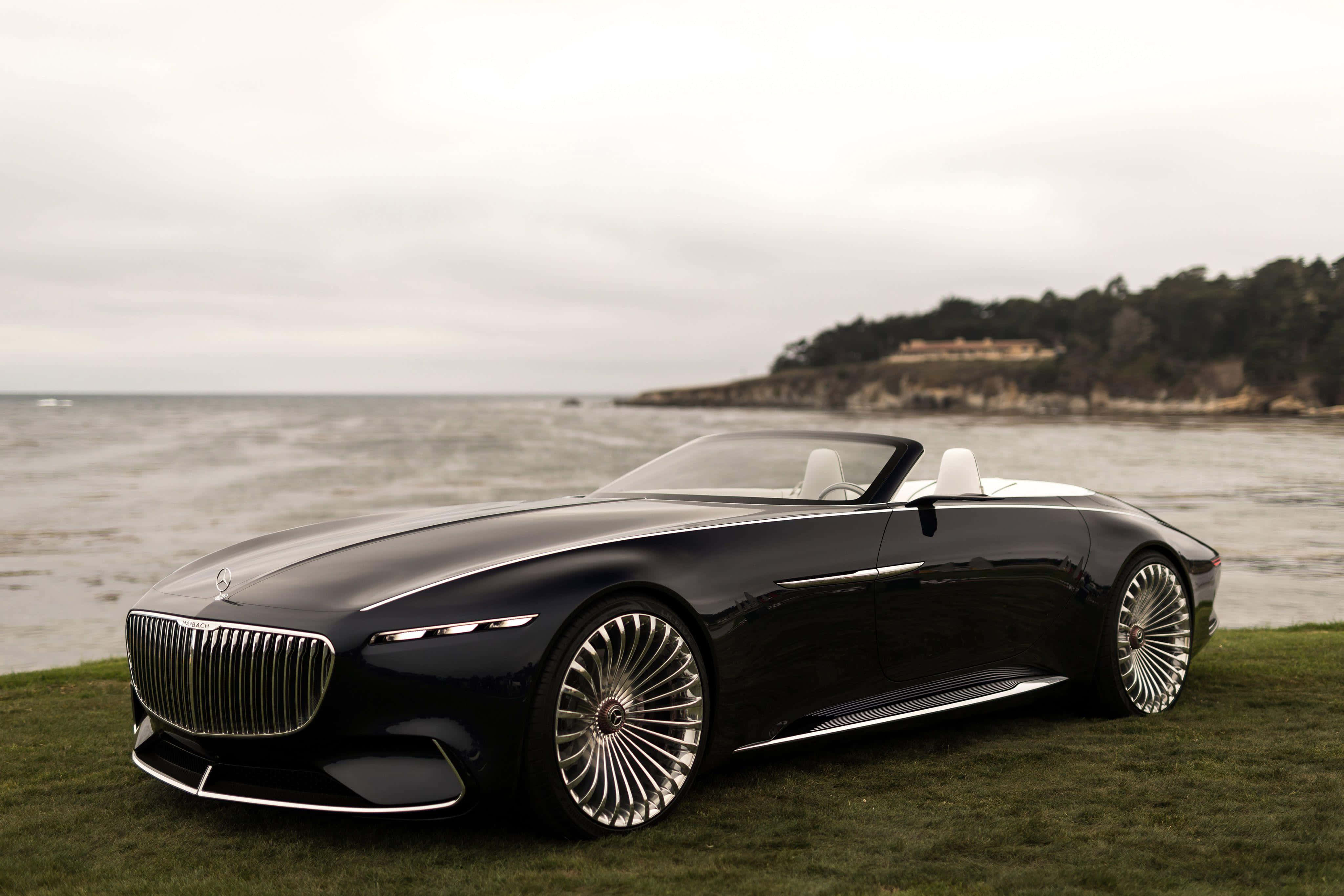 Maybach 桌布 壁紙 — 一輛時尚的黑色豪華開篷車配銀色輪圈，停泊在平靜海洋旁的草地上，天空多雲。