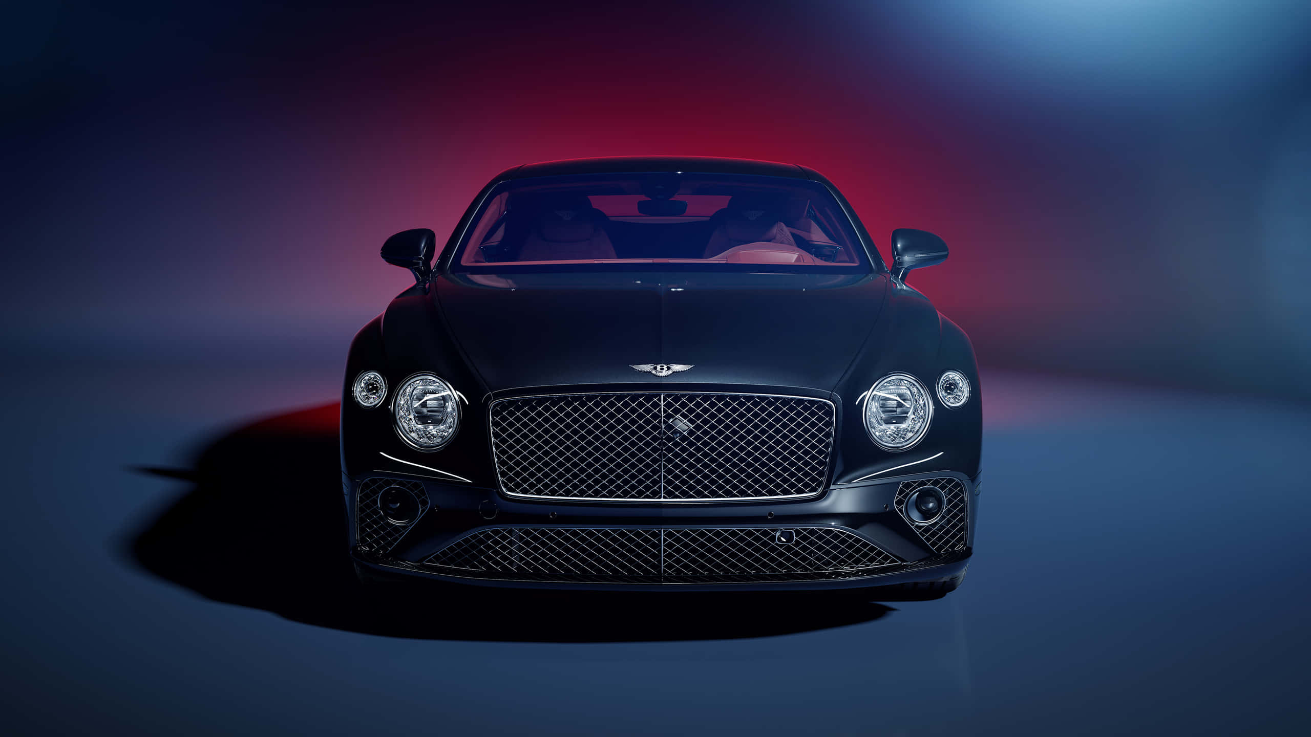 Bentley Mulsanne 桌布 壁紙 — 一輛時尚的黑色賓利 Continental GT 在戲劇性的紅色和藍色工作室燈光下正面朝前，投射出大膽的陰影。