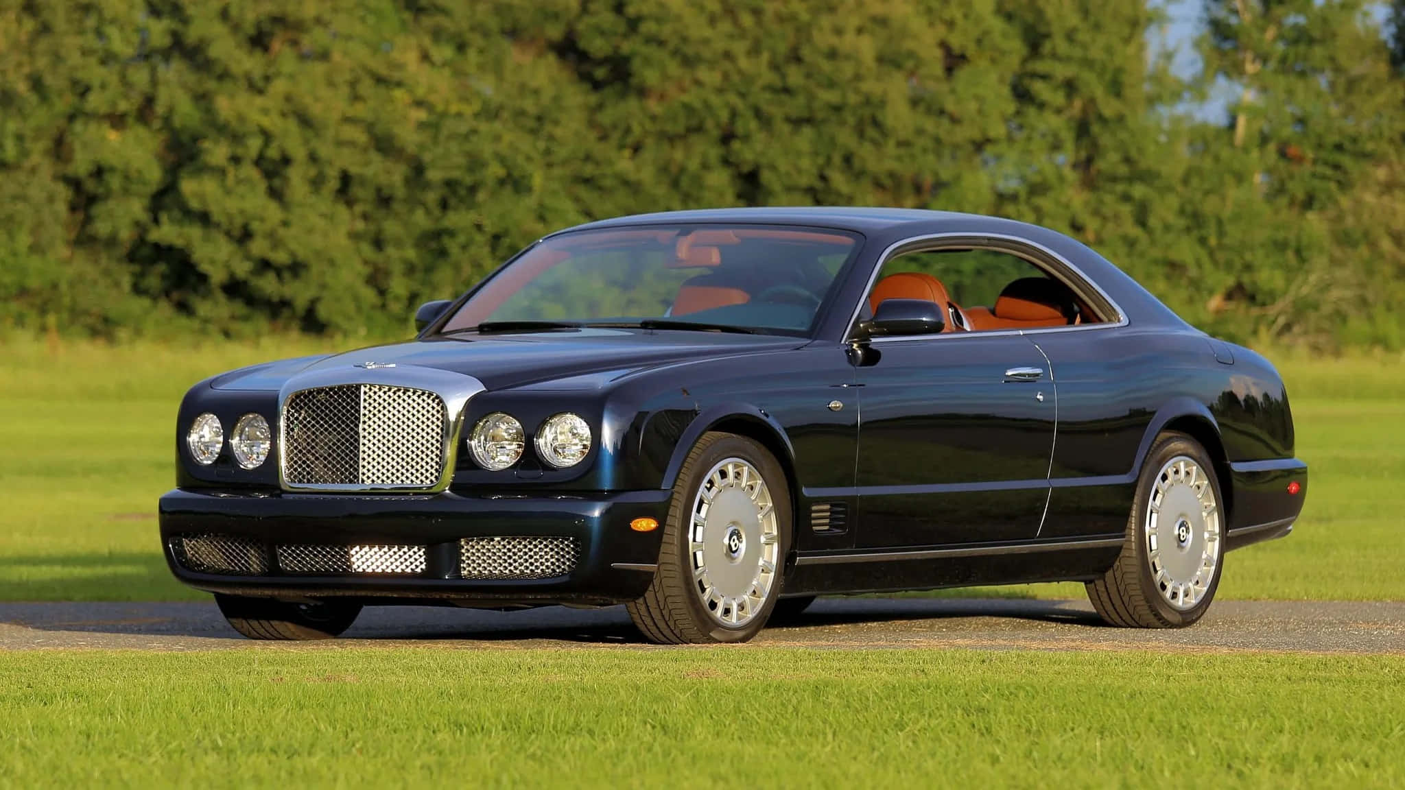 Bentley Brooklands 桌布 壁紙 — 一輛時尚的黑色賓利 Continental GT 雙門跑車停泊在碎石路上，旁邊是充滿活力的綠色草地，背景有樹木。