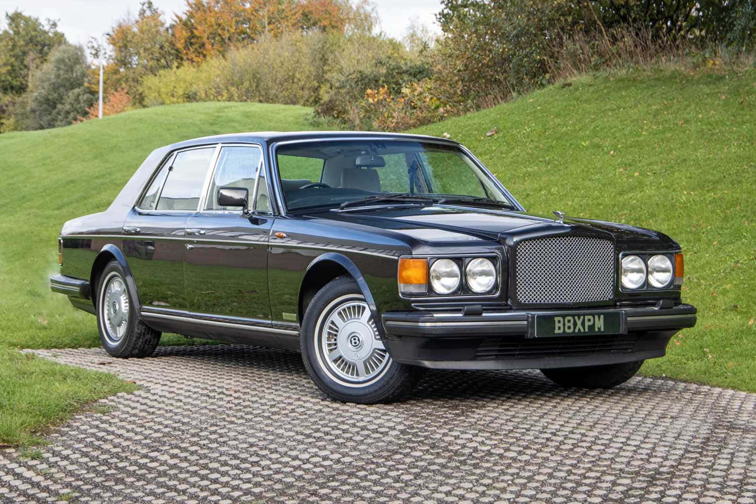 Bentley Eight 桌布 壁紙 — 一輛時尚的黑色賓利轎車停在碎石路上，旁邊是長滿青草的山丘，背景有秋天的樹木。