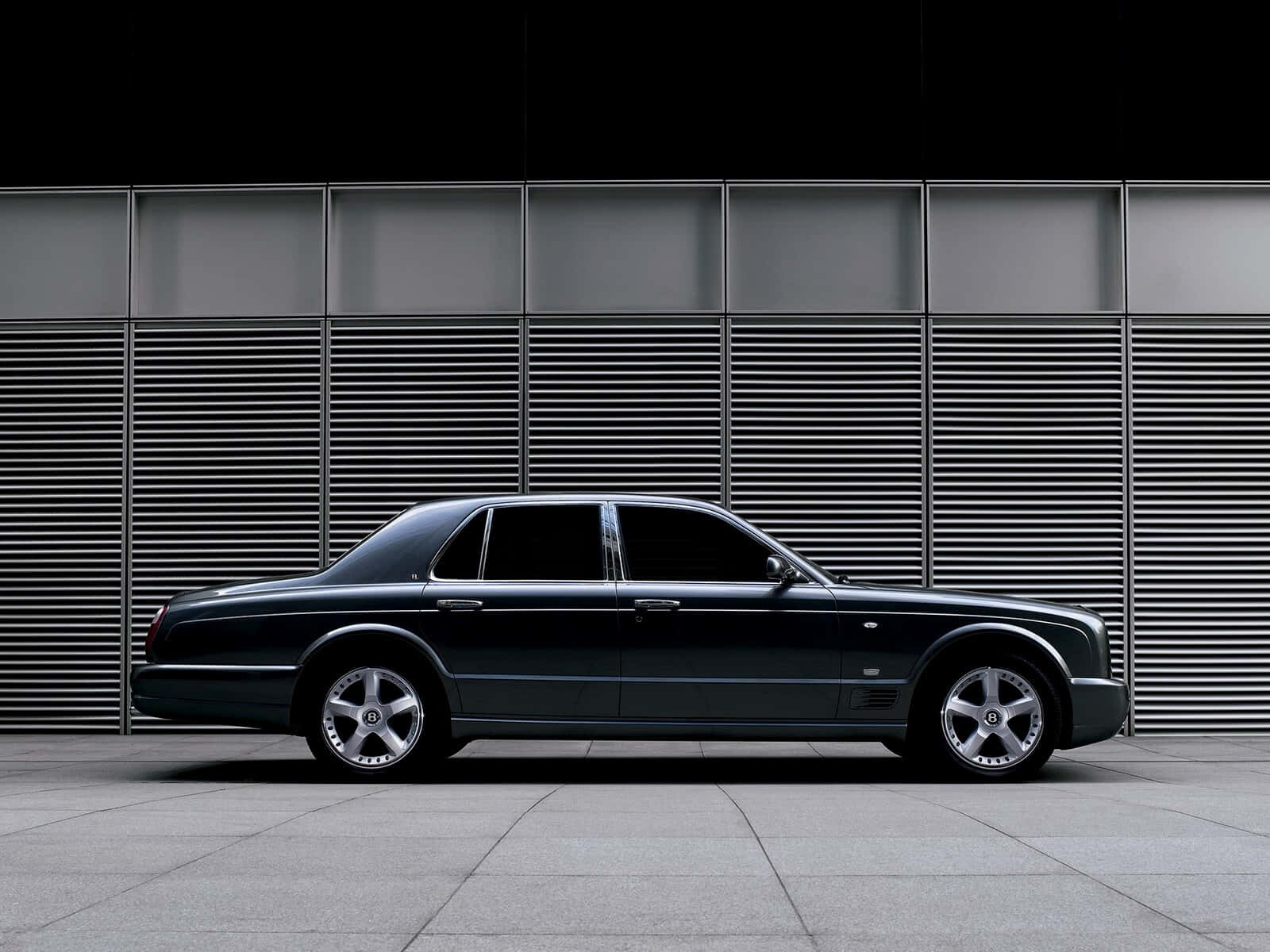 Bentley Arnage 桌布 壁紙 — 一輛時尚的黑色賓利轎車在攝影棚燈光下，側面朝向現代金屬條板牆。