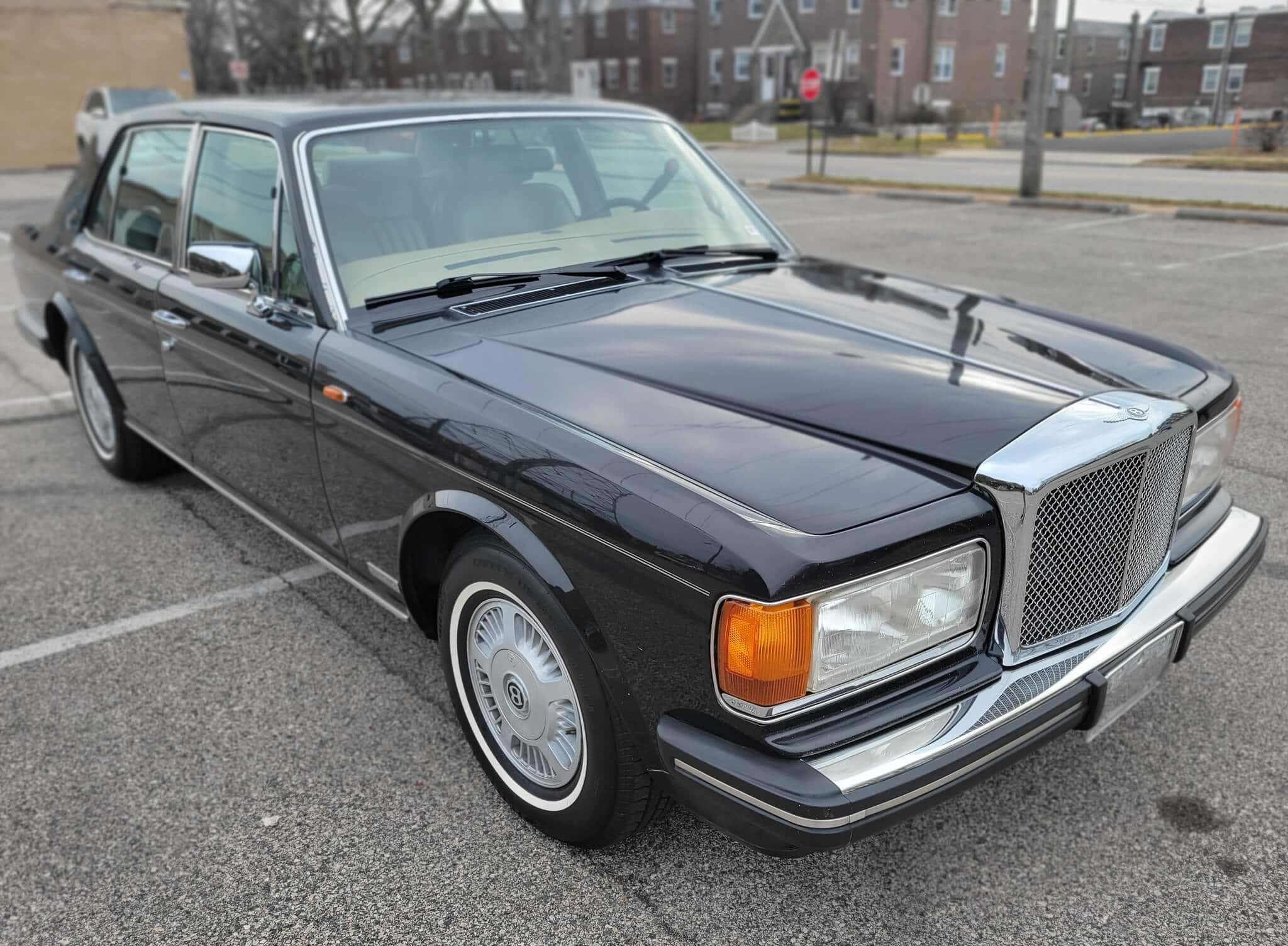 Bentley Eight 桌布 壁紙 — 一輛時尚的黑色賓利轎車在日光下閃耀，背景是城市停車場和磚砌建築。
