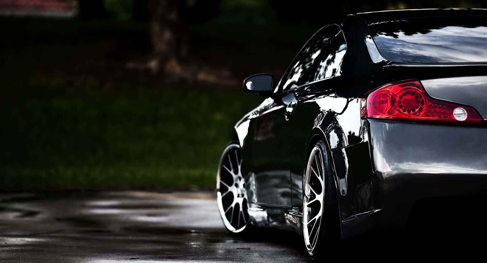 Infiniti G35 桌布 壁紙 — 一輛時尚的黑色跑車，帶有發光的紅色尾燈，停在潮濕的瀝青路上，旁邊是茂密的綠草。