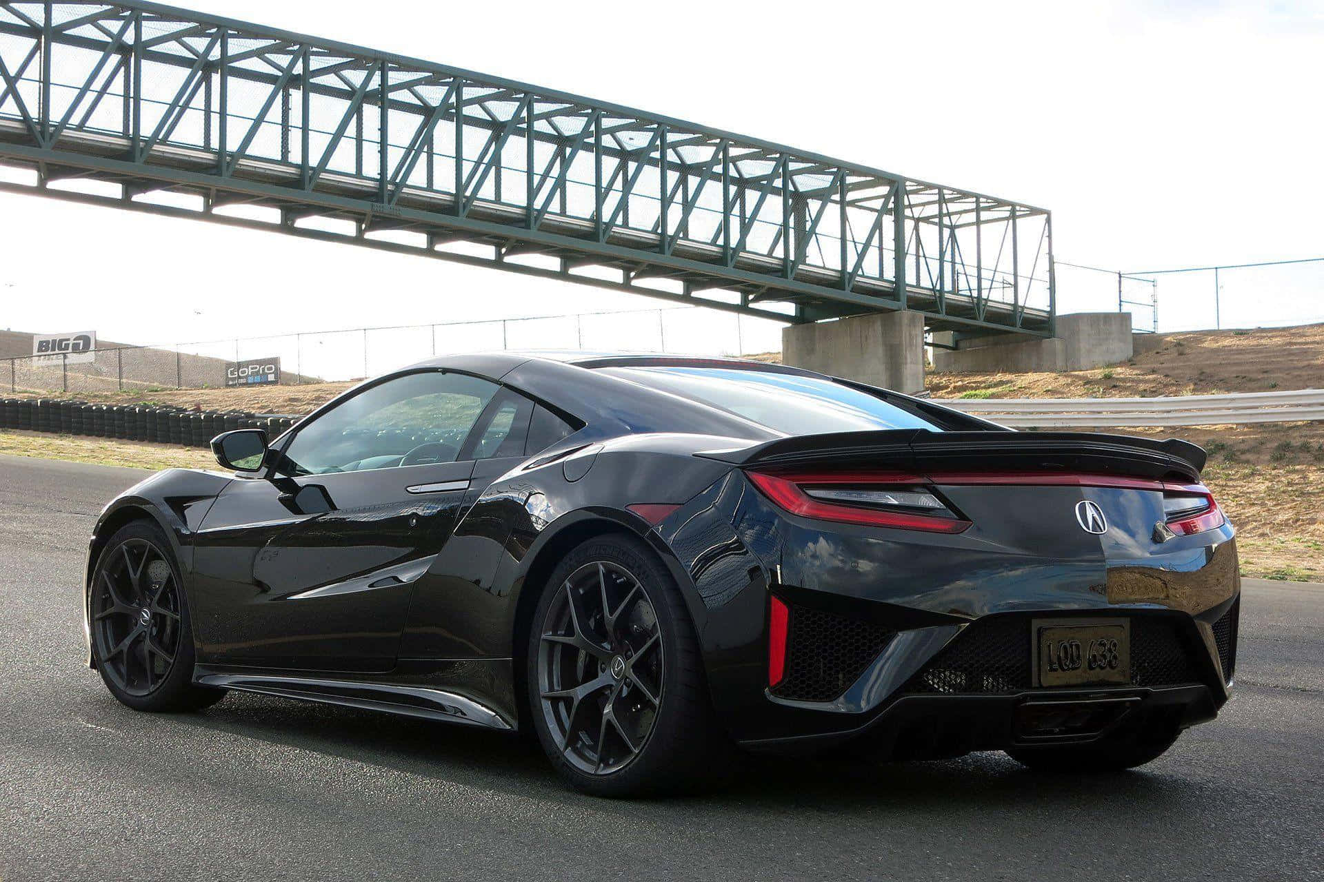 Acura Nsx 桌布 壁紙 — 一輛時尚的黑色跑車，帶有紅色尾燈，停在瀝青賽道上的綠色金屬橋下。