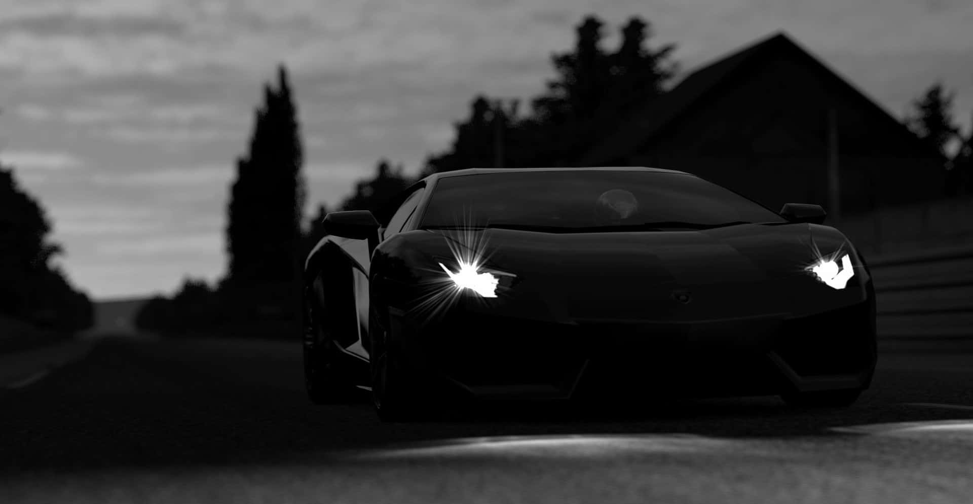 Black And White Car 桌布 壁紙 — 一輛時尚的黑色跑車，配備發光的車頭燈，在黃昏時分行駛在一條燈光昏暗的道路上，背景有樹木和一間房屋。