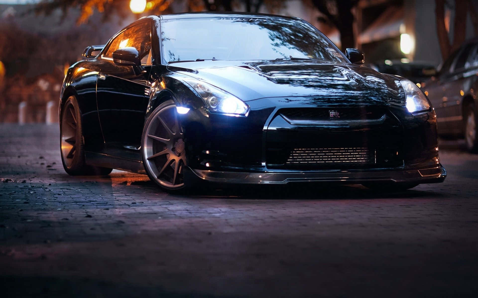 Jdm Car 桌布 壁紙 — 一輛時尚的黑色跑車在夜晚濕漉漉的鵝卵石街道上，在街燈下閃閃發光。