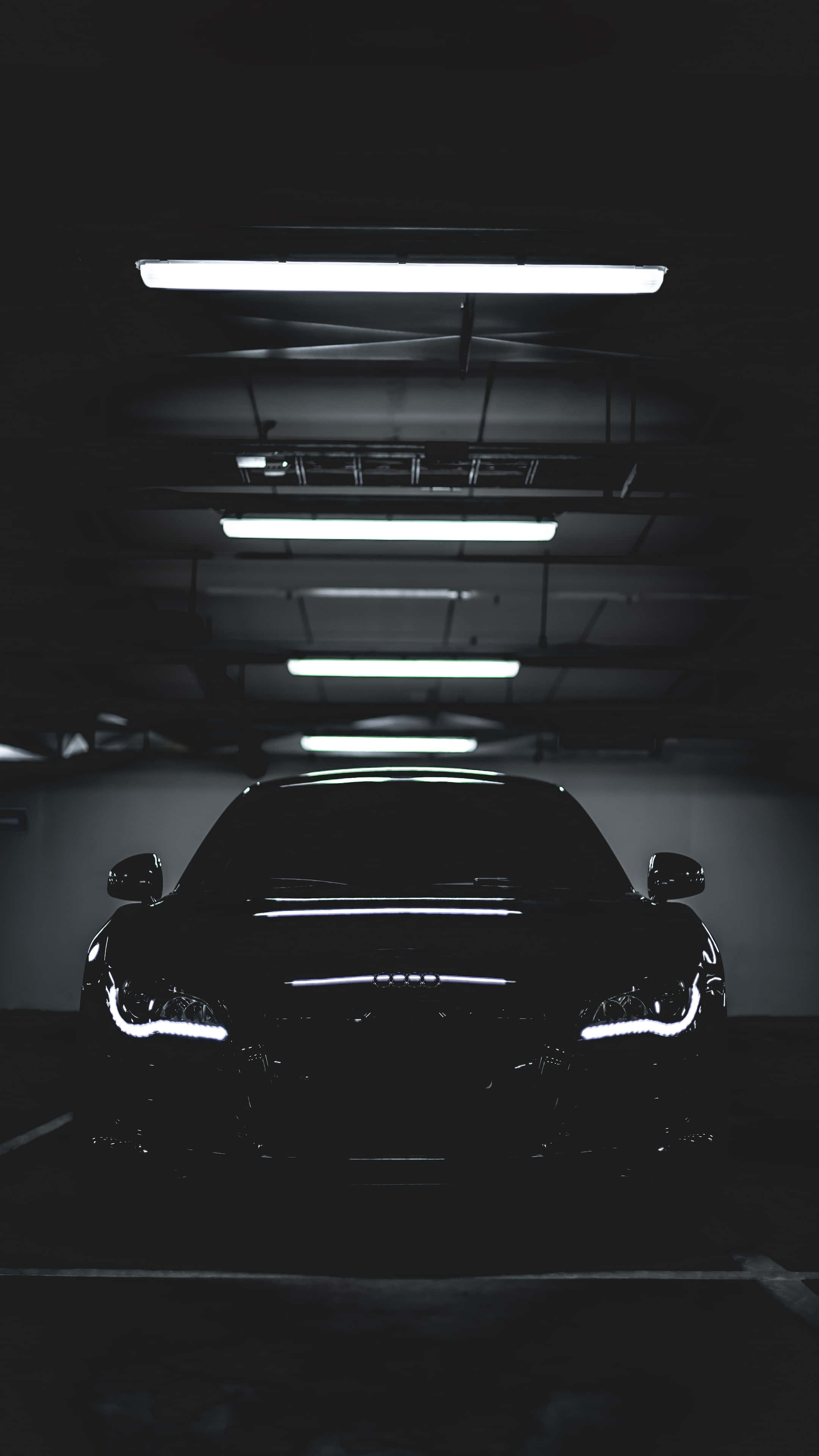 4K Car 桌布 壁紙 — 一輛時尚的黑色跑車在燈光昏暗的地下停車場中閃爍著亮起的車頭燈。