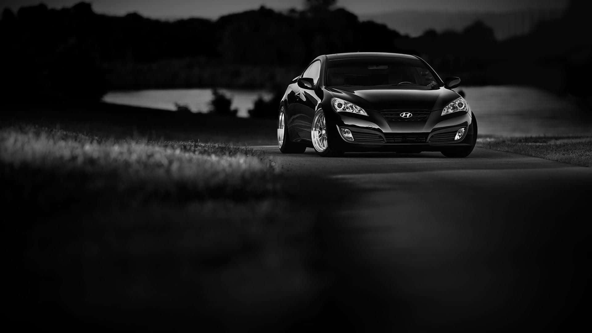 Hyundai Genesis 桌布 壁紙 — 一輛時尚的黑色跑車在黃昏時沿著蜿蜒的道路行駛，背景是模糊的草地和黑暗的樹線。