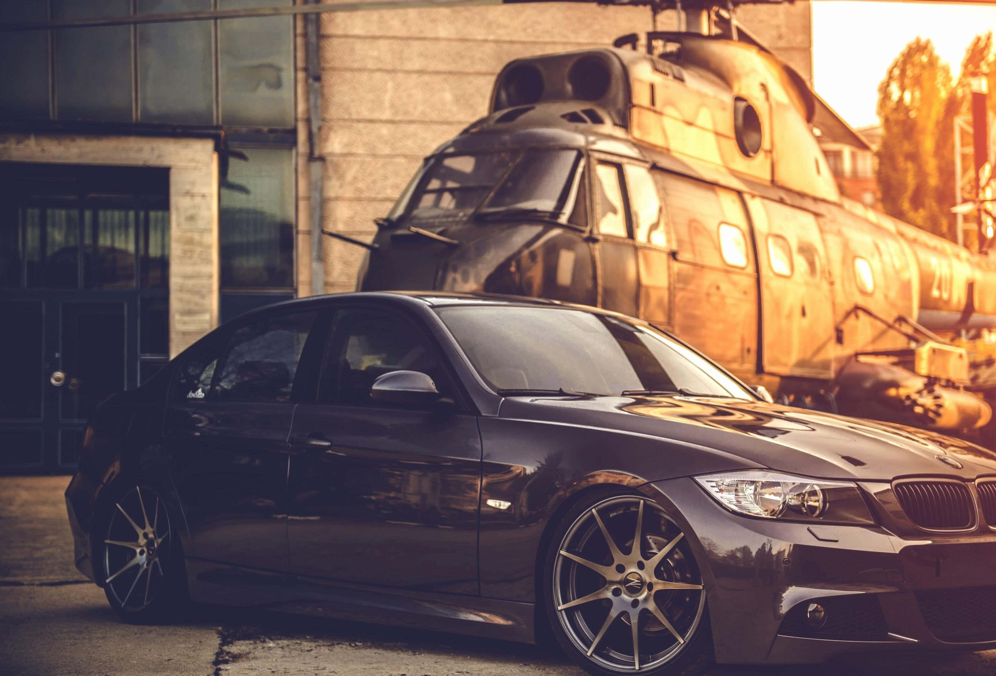 Tuned Car 桌布 壁紙 — 一輛時尚的黑色跑車配金色輪圈，停在生鏽的復古火車前，沐浴在溫暖的黃金時刻光線中。